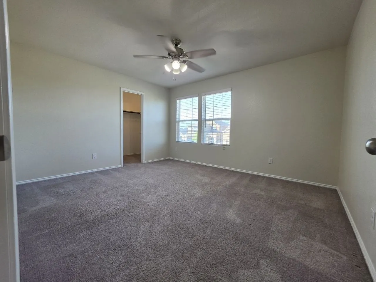 Neutral-toned wall paint, two windows with blinds, ceiling fan with integrated lighting, and carpet flooring