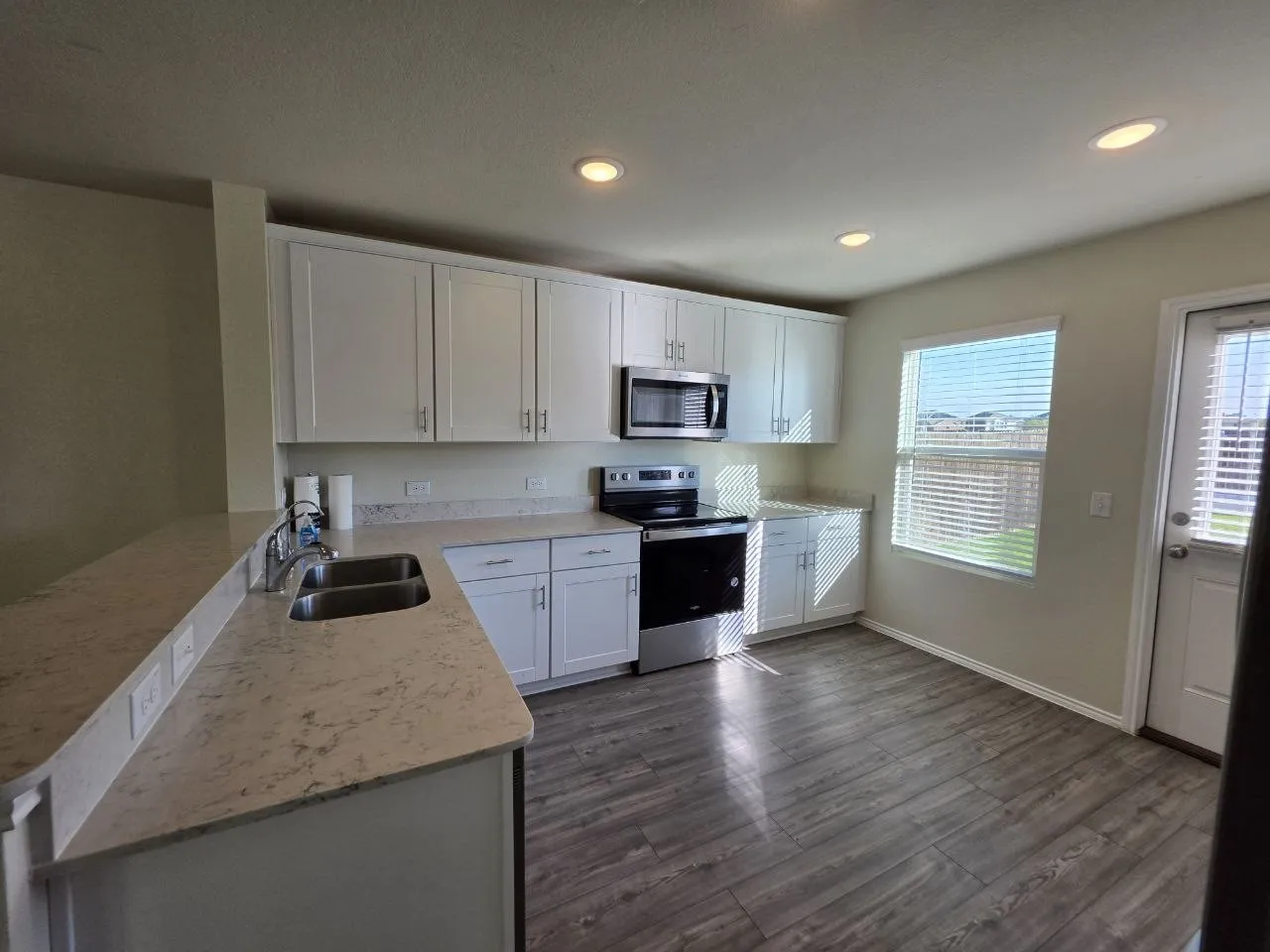 Kitchen featuring white shaker cabinetry, stainless steel appliances, light-toned countertops, wood-finish flooring, and recessed lighting