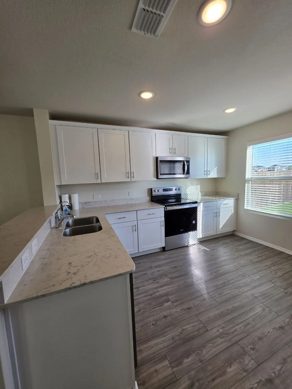 Kitchen featuring white shaker cabinetry, stainless steel appliances, light-toned countertops, a double basin sink, and wood-finish flooring
