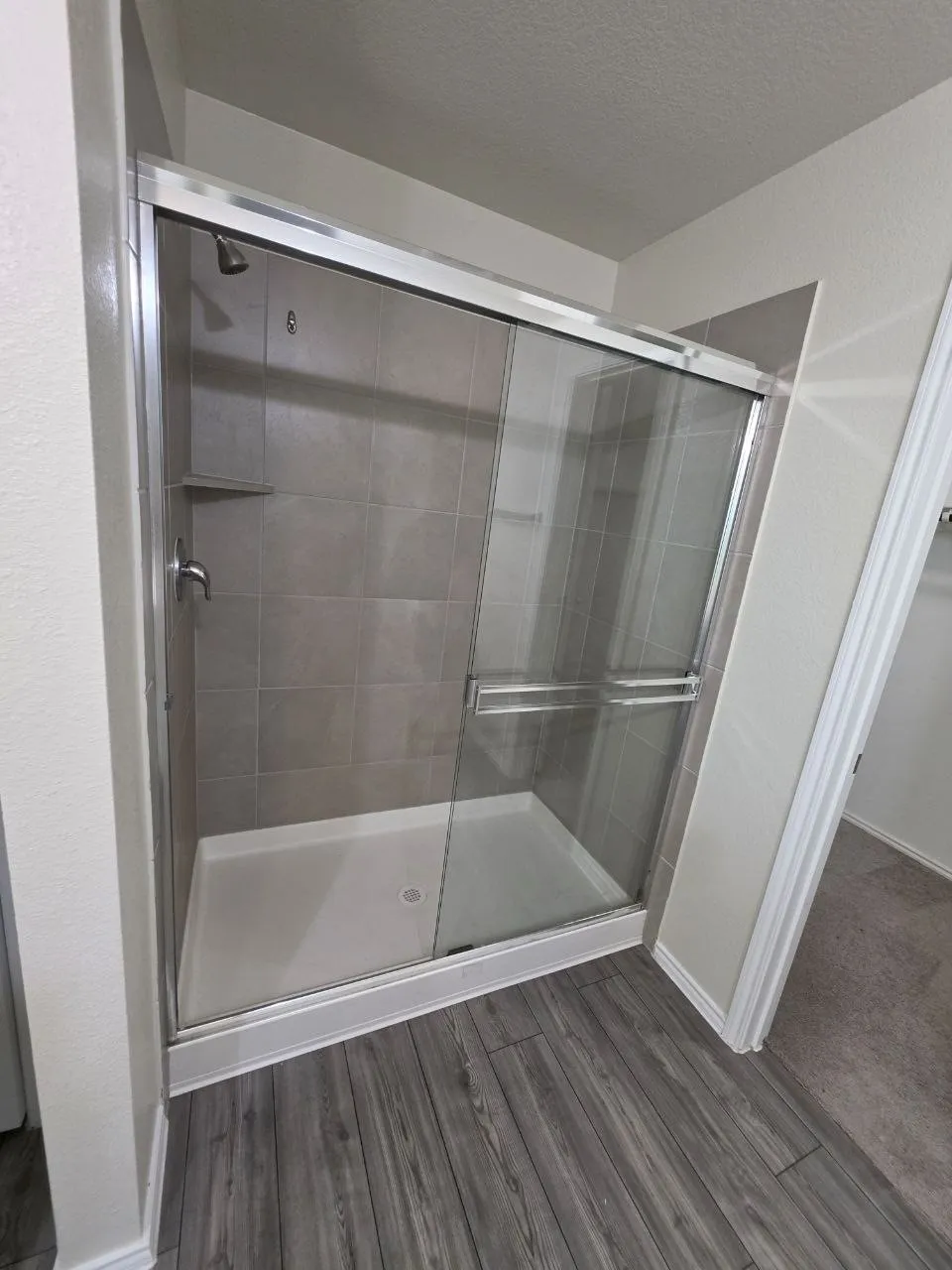 Glass-enclosed shower with a gray tiled surround, built-in shelf, and a white shower pan