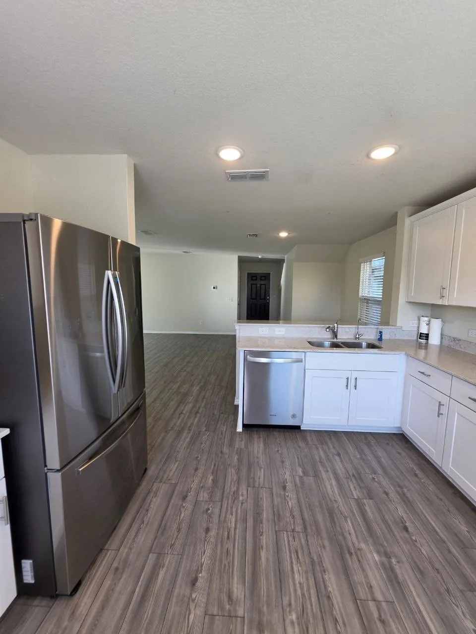 Kitchen featuring wood-finish flooring, stainless steel appliances, white cabinetry, light-toned countertops, and recessed lighting
