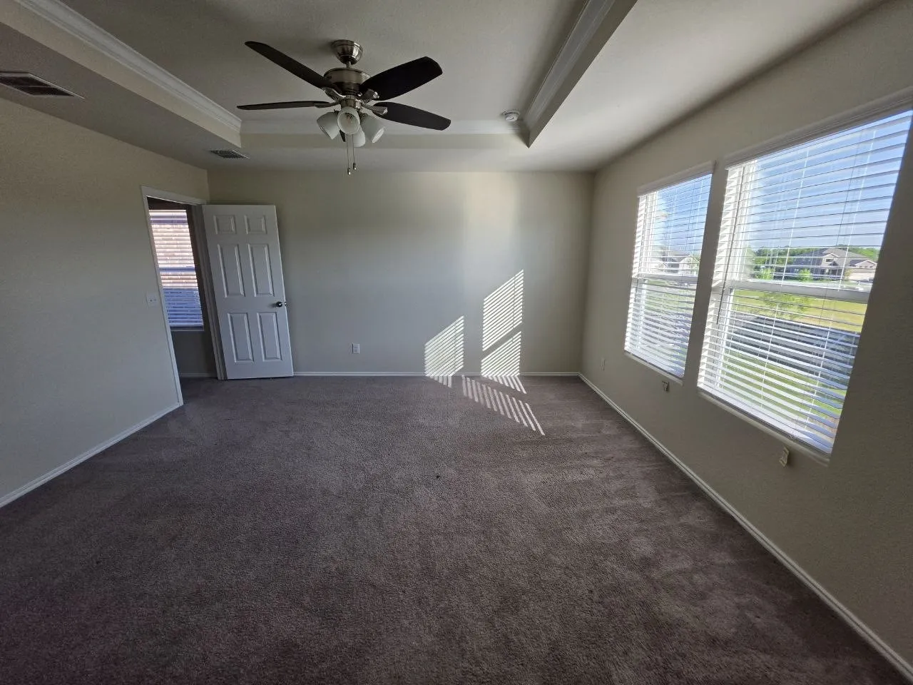 Recessed tray ceiling with crown molding, ceiling fan with light fixture, carpeted flooring, and multiple windows