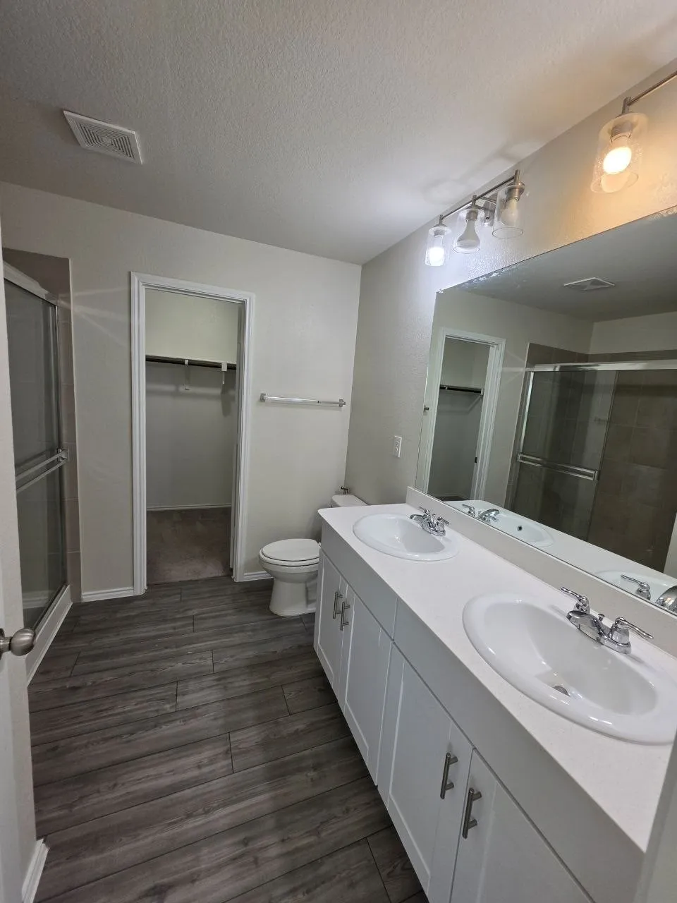 Dual vanity with under-sink storage, wood-finish flooring, glass-enclosed shower, and built-in closet shelving