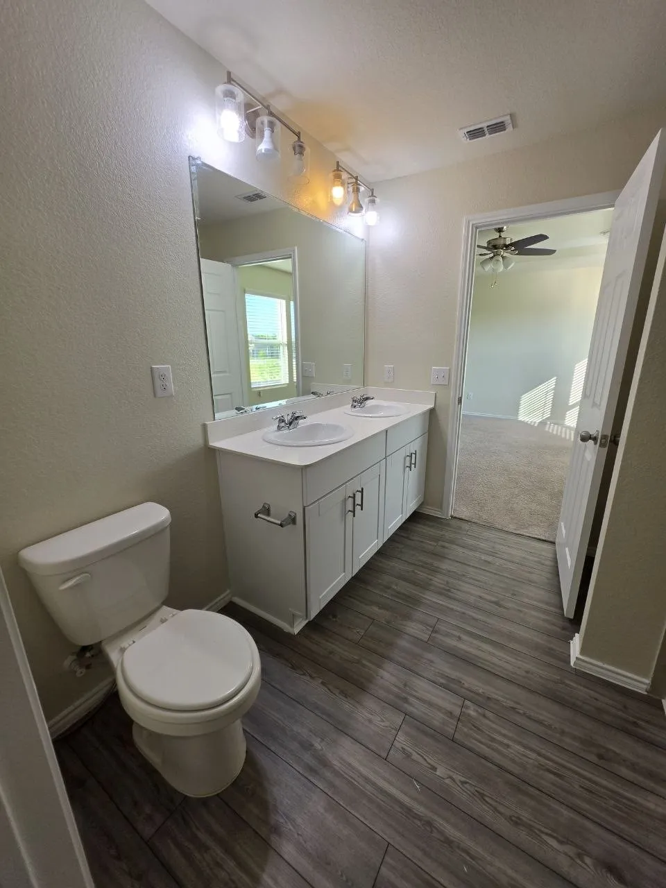 Dual sink vanity with white cabinetry, wood-finish flooring, full-width mirror, and overhead track lighting