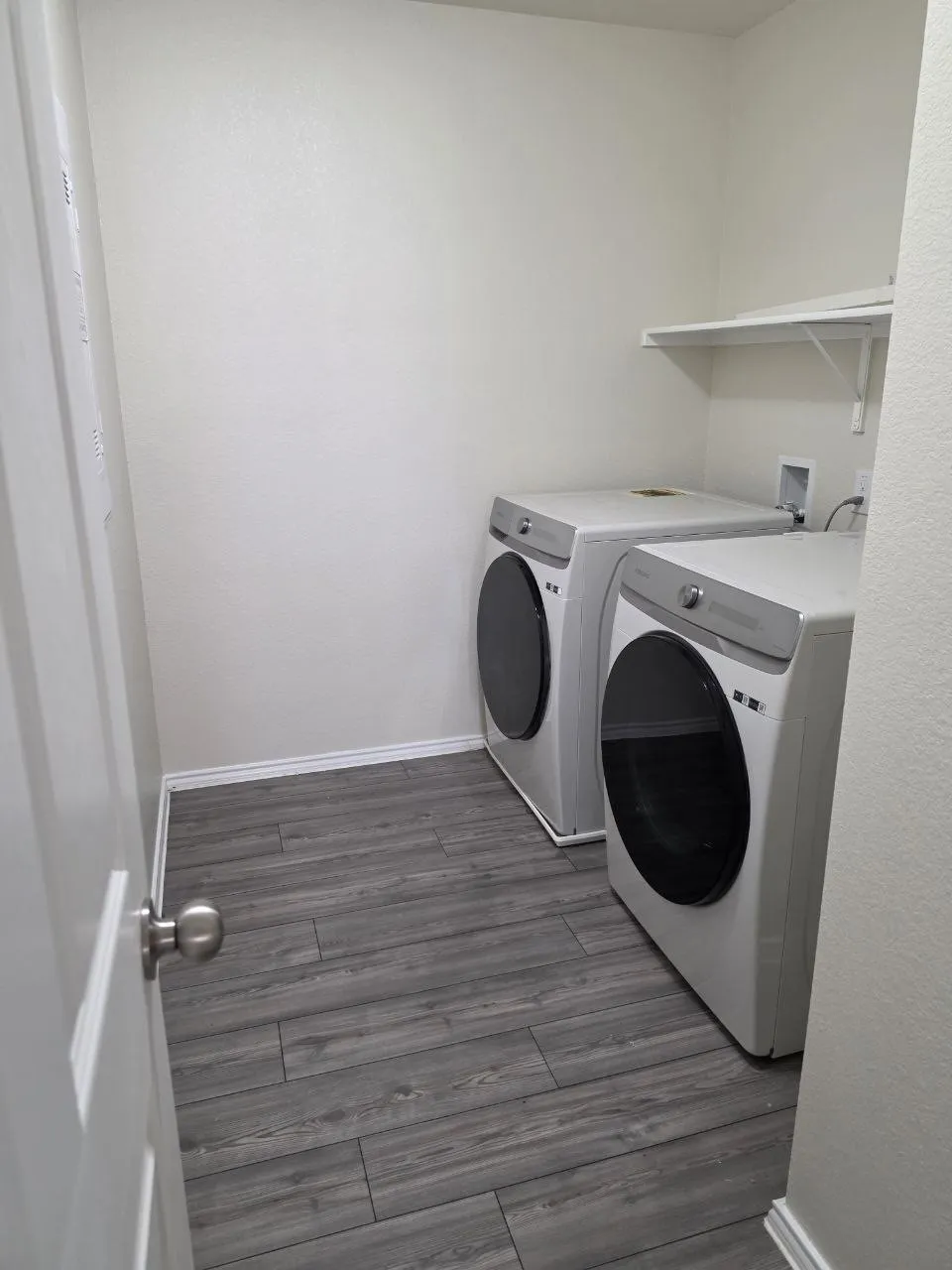 Wood-finish flooring with white baseboards, a wall-mounted shelving unit, and white walls