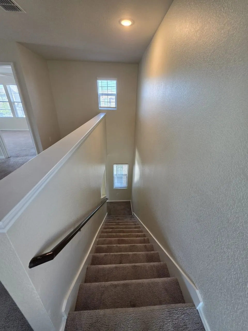 Carpeted staircase with a dark handrail, neutral painted walls, and recessed lighting