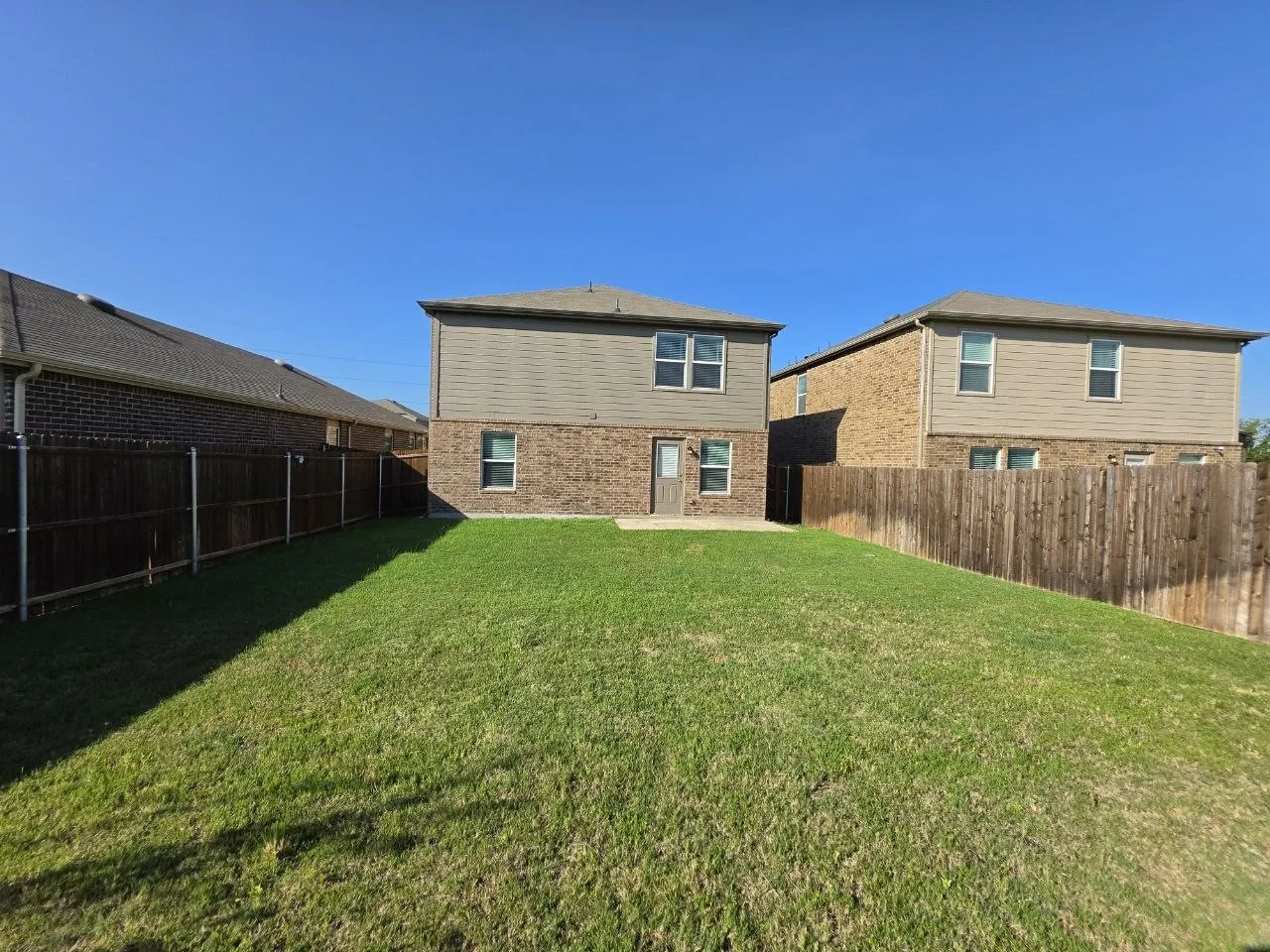 Expansive backyard with a manicured lawn, full privacy fencing, and a concrete patio