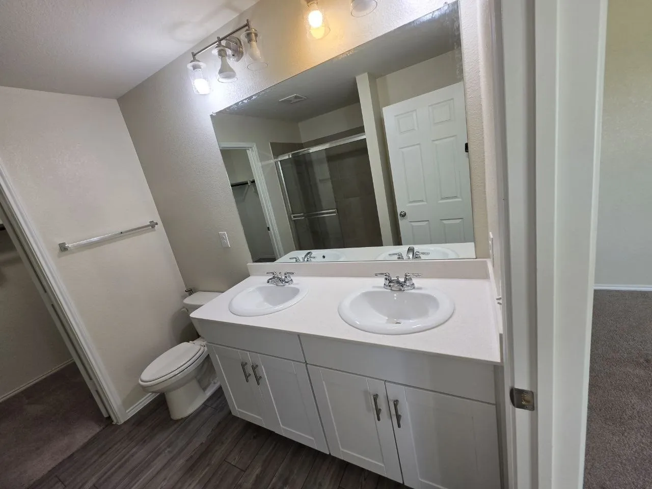 Dual vanity with white cabinetry, wood-finish flooring, and a large wall-mounted mirror