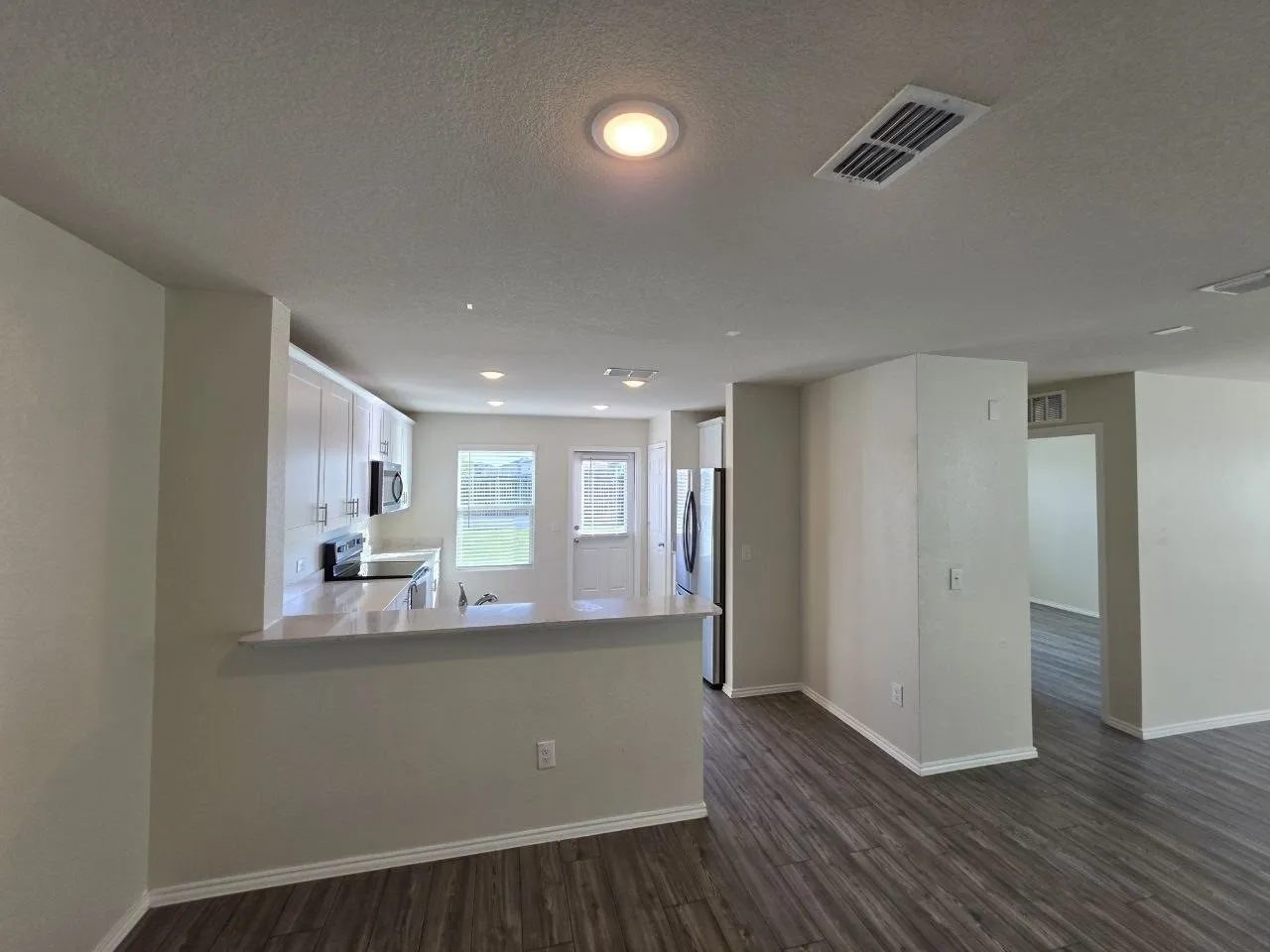 Open-concept kitchen with wood-finish flooring, white cabinetry, integrated appliances, and a breakfast bar
