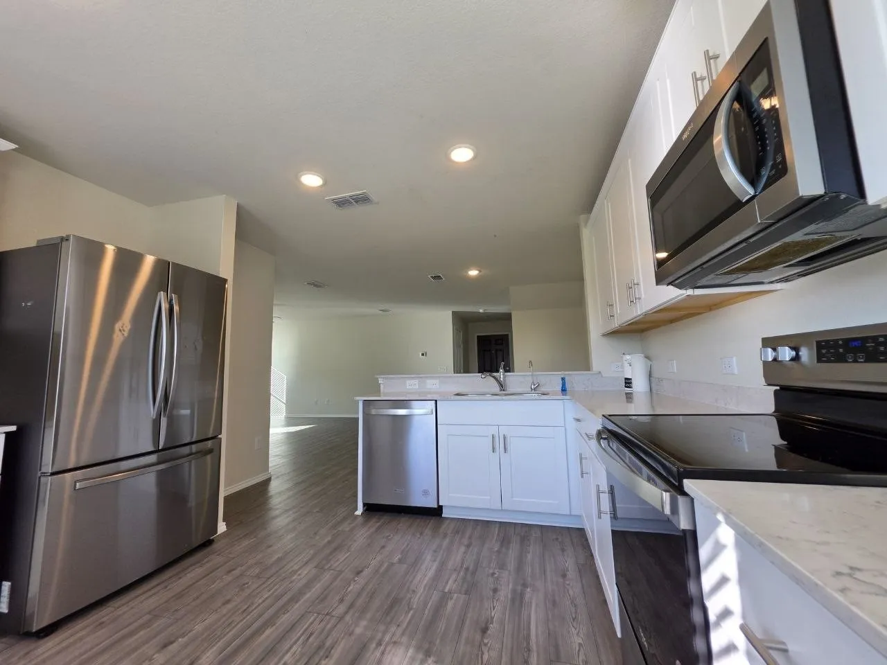 Kitchen featuring stainless steel appliances, white cabinetry, integrated sink, light-toned countertops, and wood-finish flooring