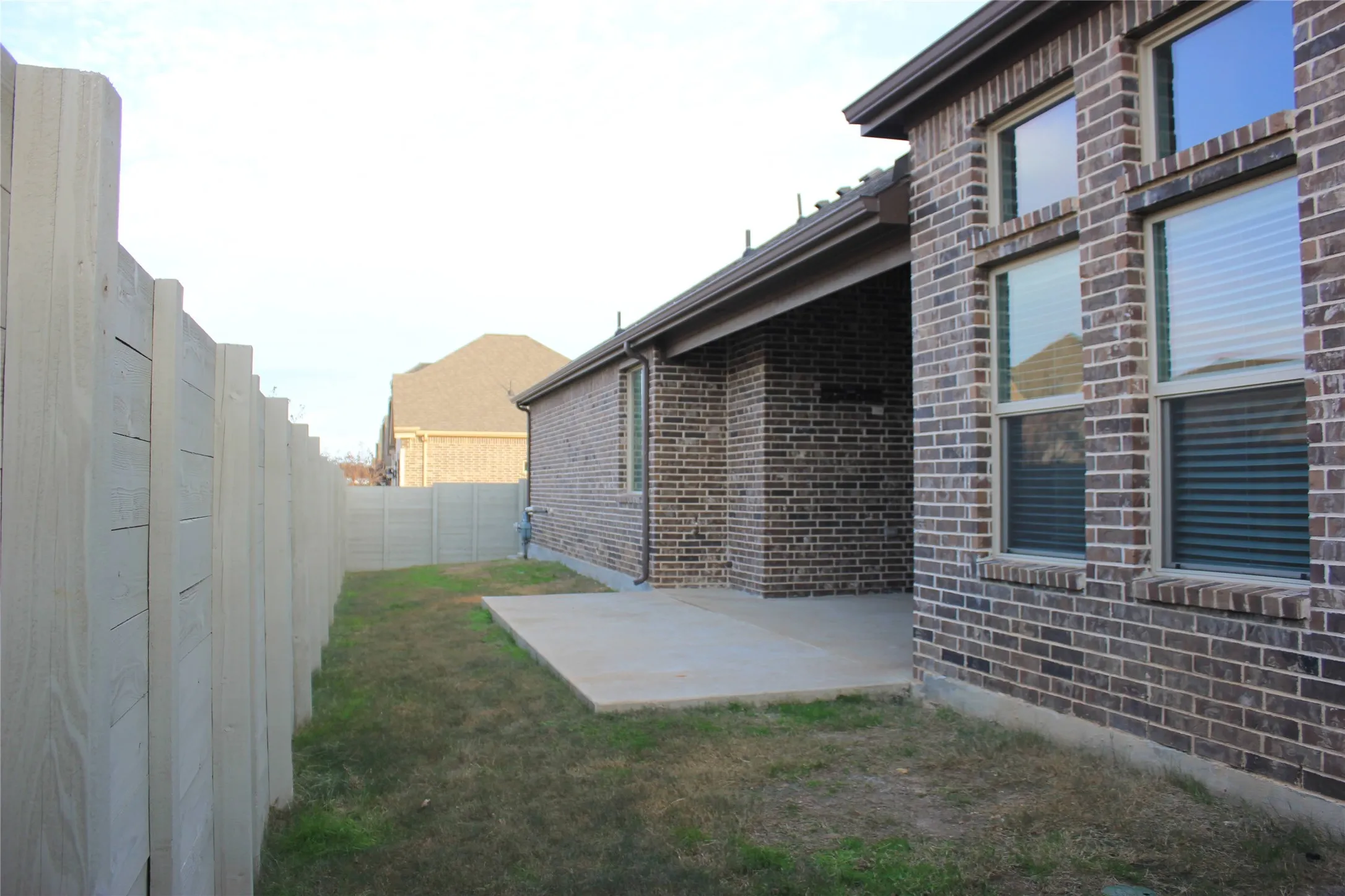 Brick exterior with multiple windows, covered patio, concrete patio pad, and a privacy fence
