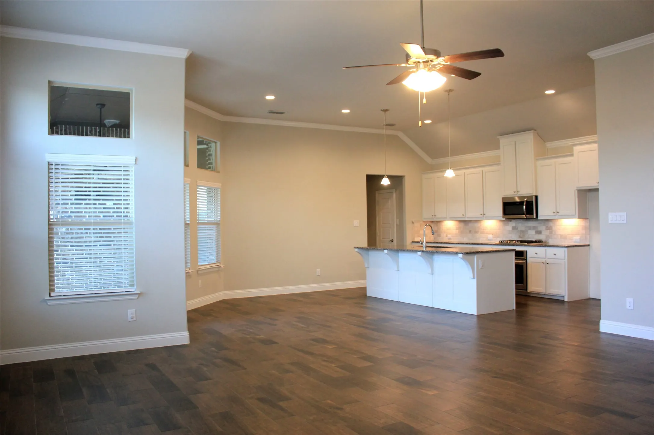 Open-concept living area featuring wood-look flooring, vaulted ceilings, recessed lighting, and a kitchen with an island and white cabinetry
