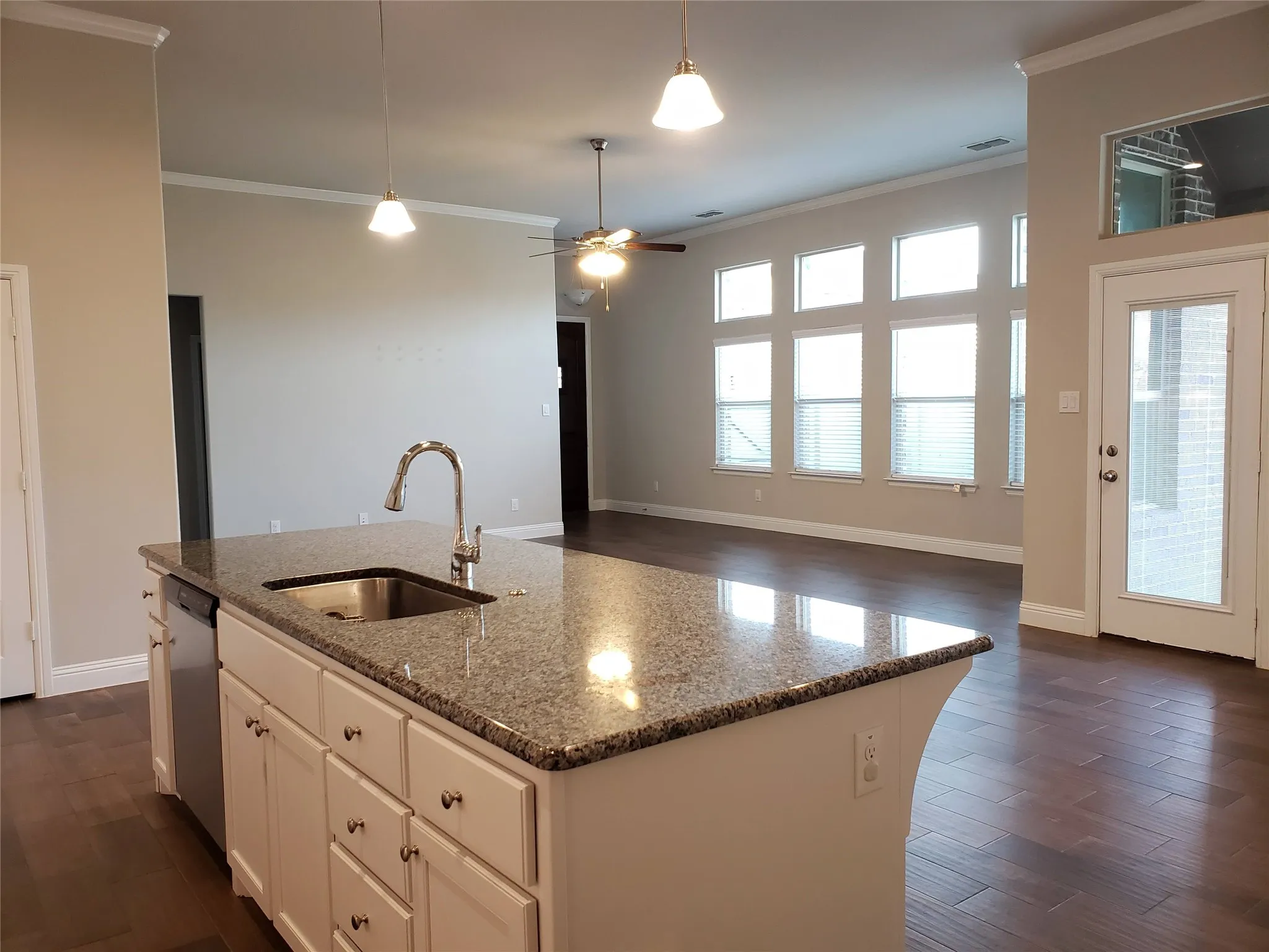 Kitchen island with granite countertop and undermount sink, stainless steel dishwasher, wood-finish flooring, and multiple transom windows