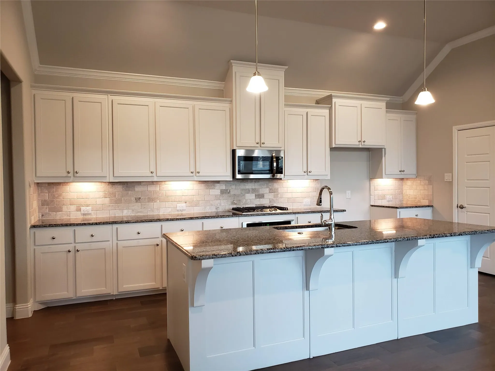 Kitchen featuring white cabinetry, dark stone countertops, tile backsplash, stainless steel appliances, and a central island with an undermount sink