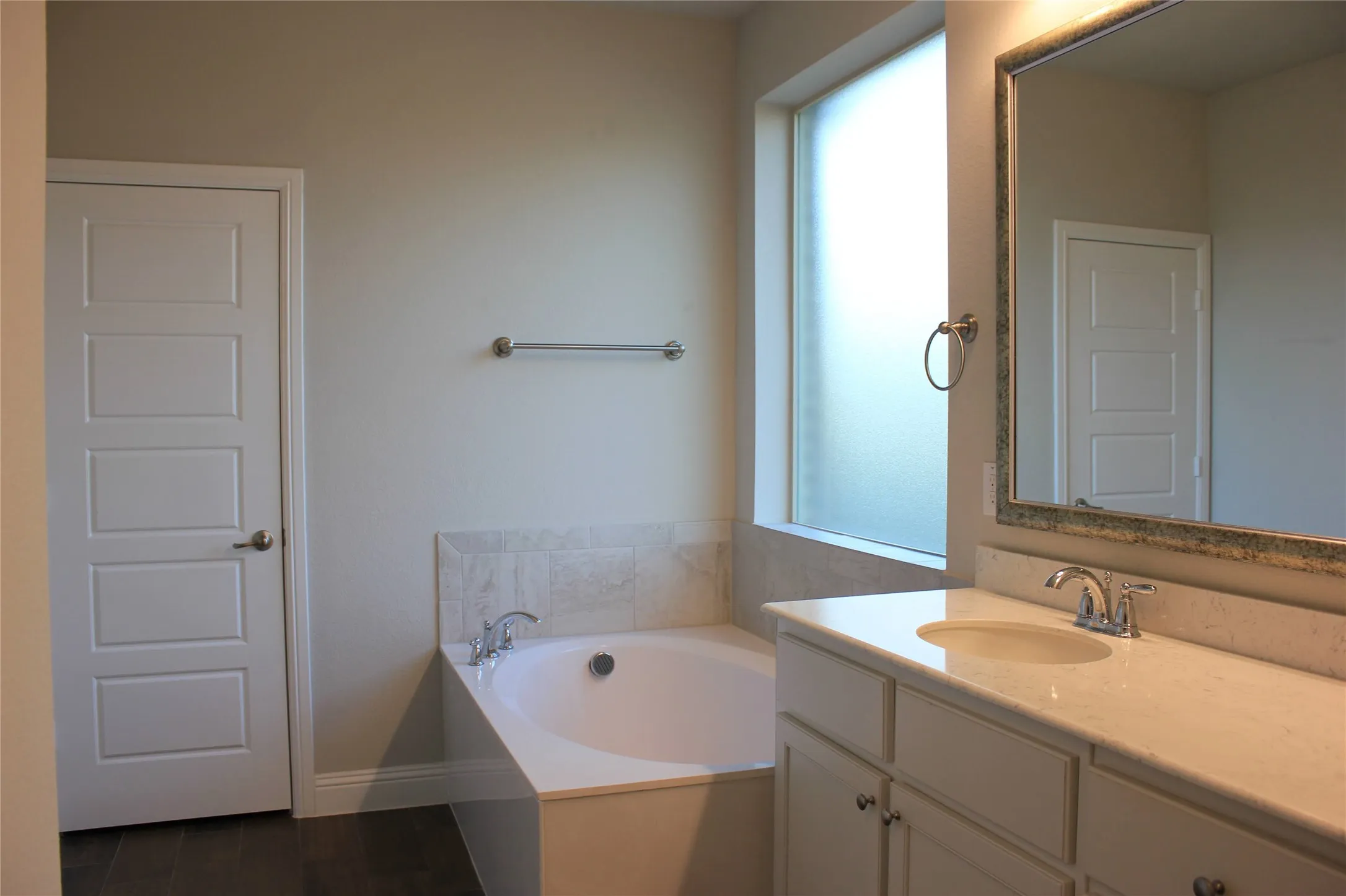 Primary Bath Built-in soaking tub with tile surround, frosted privacy window, vanity with integrated sink, and framed mirror
