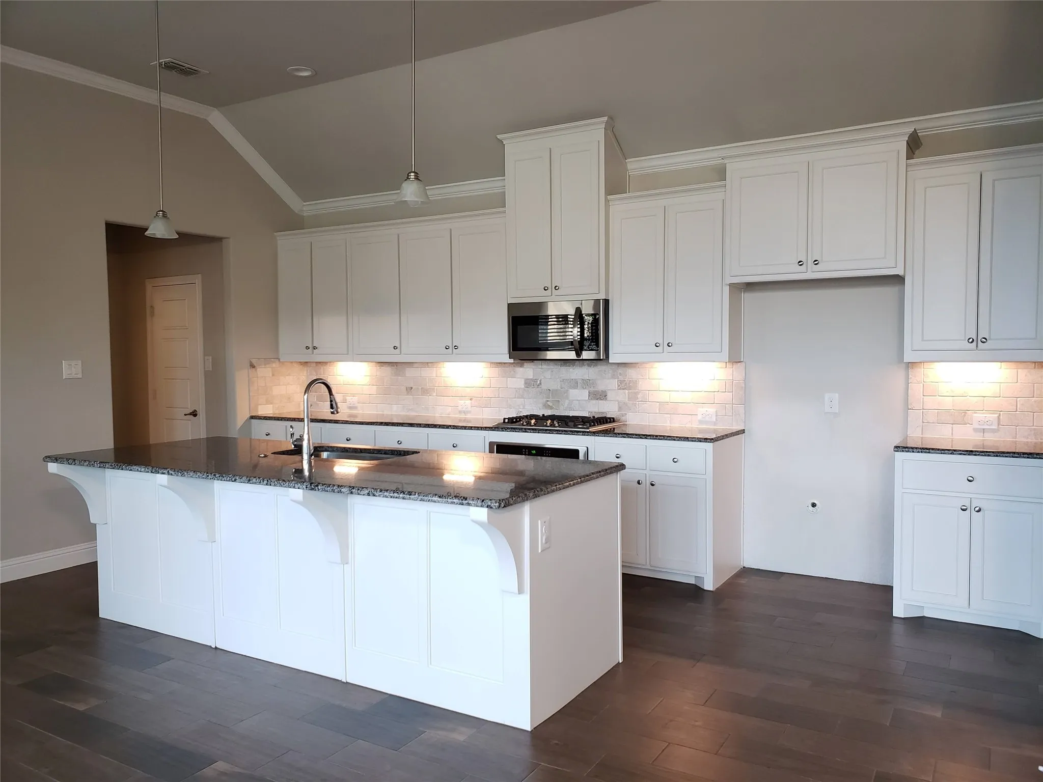 Open-concept kitchen with a vaulted ceiling, wood-finish flooring, white cabinetry, granite countertops, and a subway tile backsplash