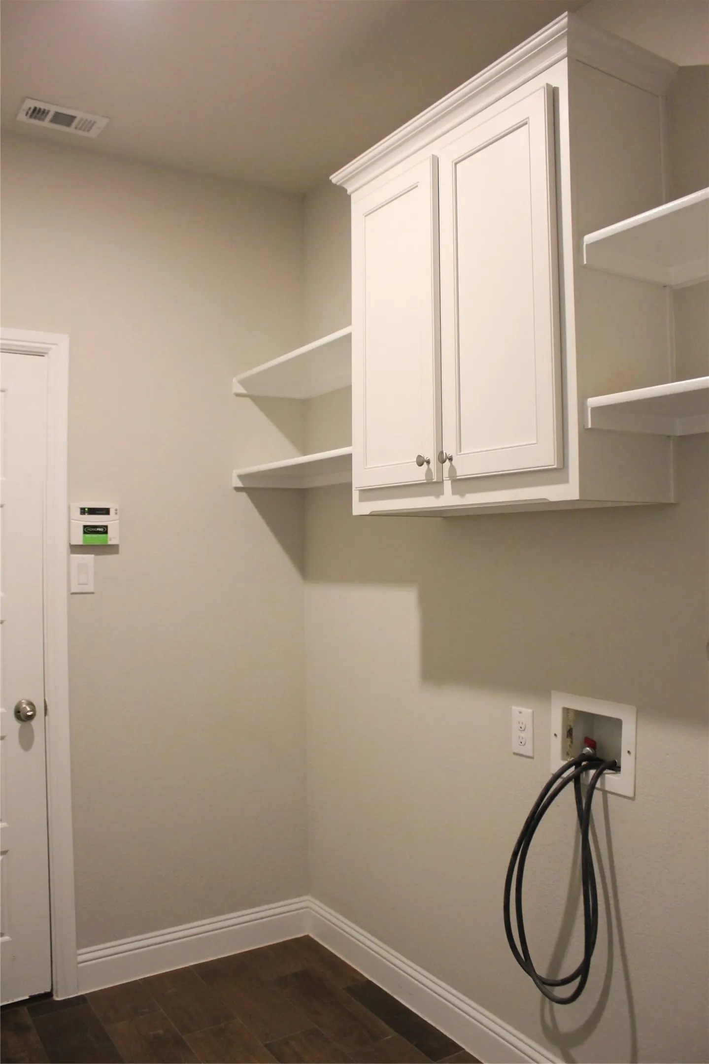 Utility room with White shaker-style cabinetry with crown molding, integrated wall shelving, wood-finish flooring, and a laundry hookup station