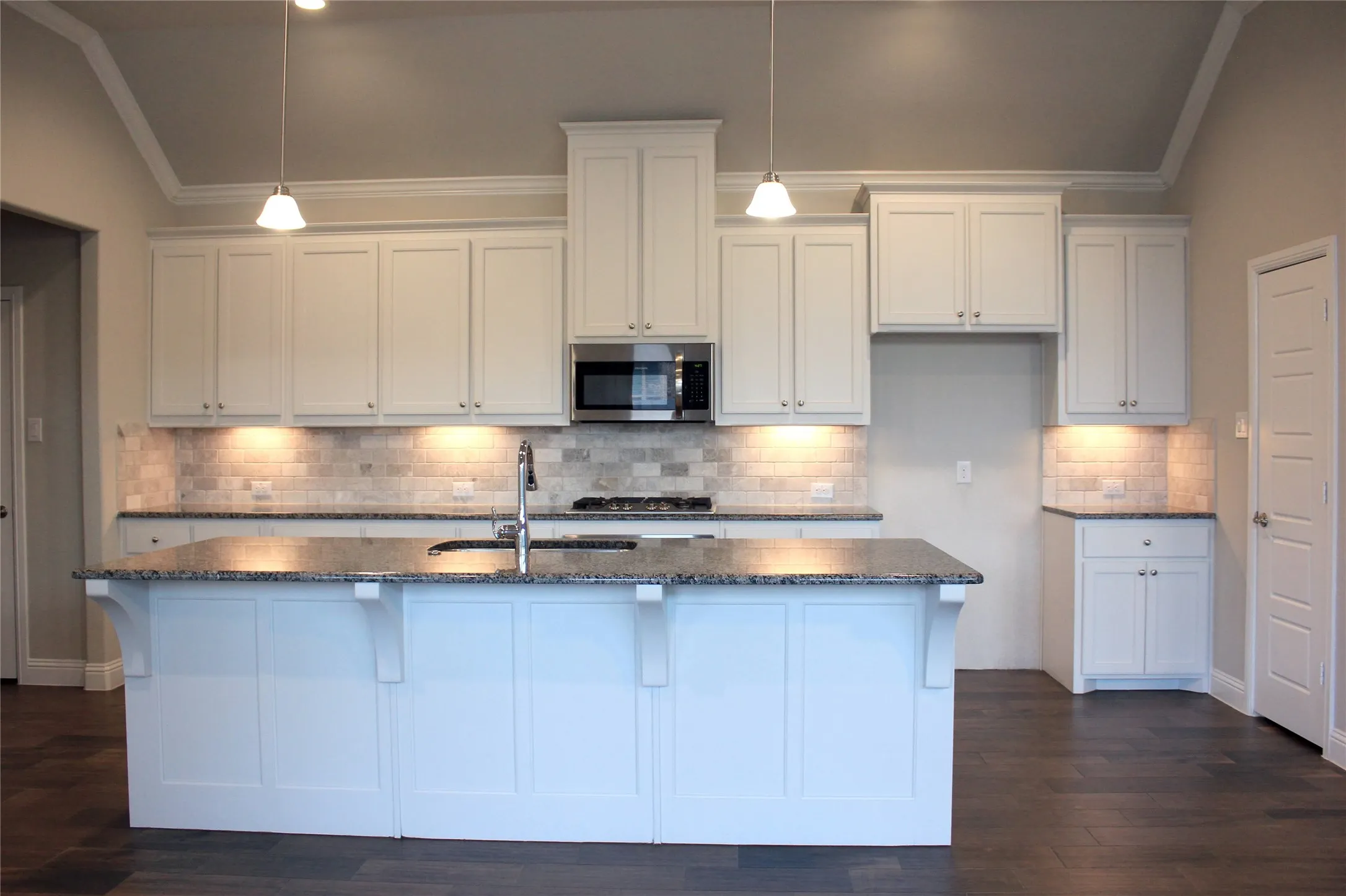 Kitchen featuring white shaker cabinetry, granite countertops, tile backsplash, stainless steel microwave, and wood-finish flooring