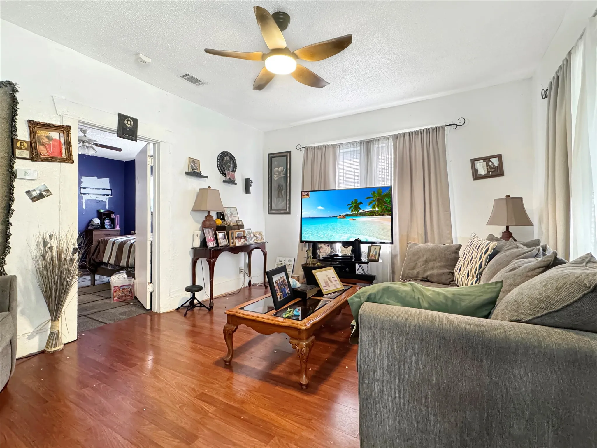 Wood-finish flooring throughout, ceiling fan with integrated lighting, and multiple windows with curtain rods