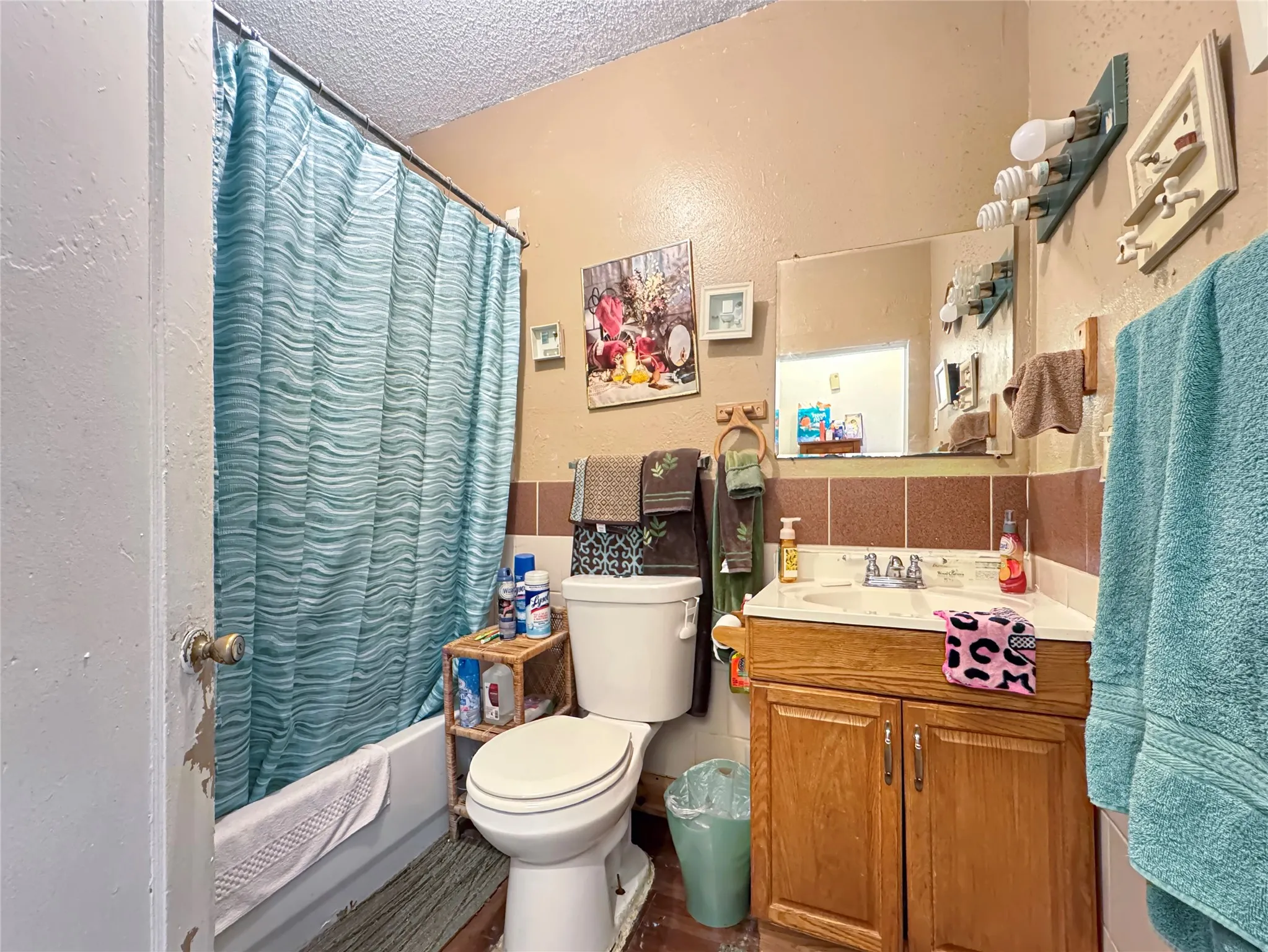 Built-in bathtub with shower, toilet, wood-finish vanity with integrated sink, wall-mounted mirror, and tiled wainscoting