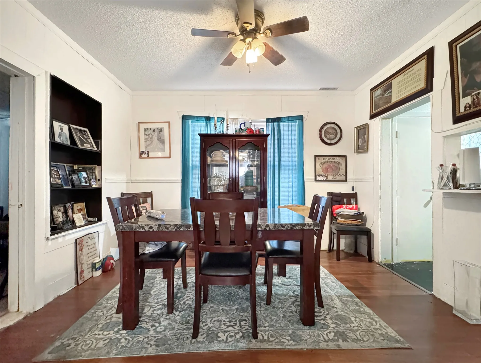Wood-finish flooring, built-in shelving, ceiling fan with integrated lighting, and white trim molding