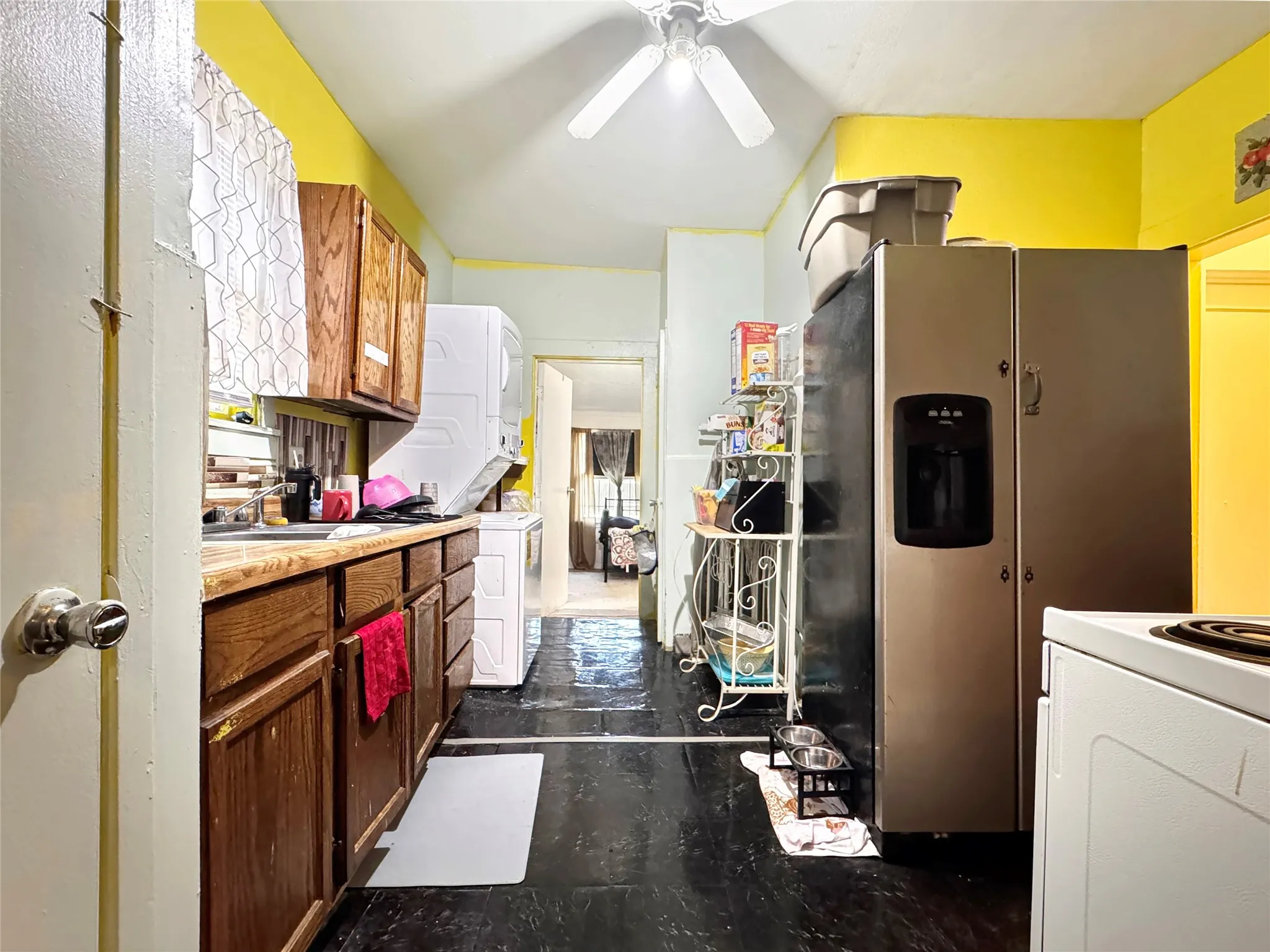 Wood-finish cabinetry and countertops, stacked washer and dryer unit, and stainless steel refrigerator with integrated ice and water dispenser