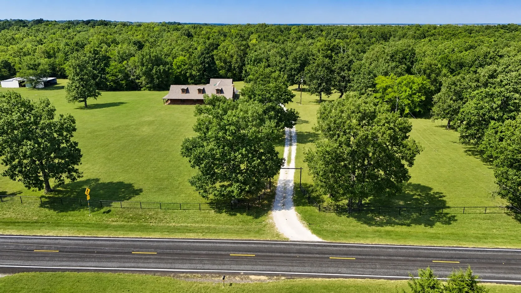 Expansive property featuring a gravel driveway, mature trees, and a distant outbuilding
