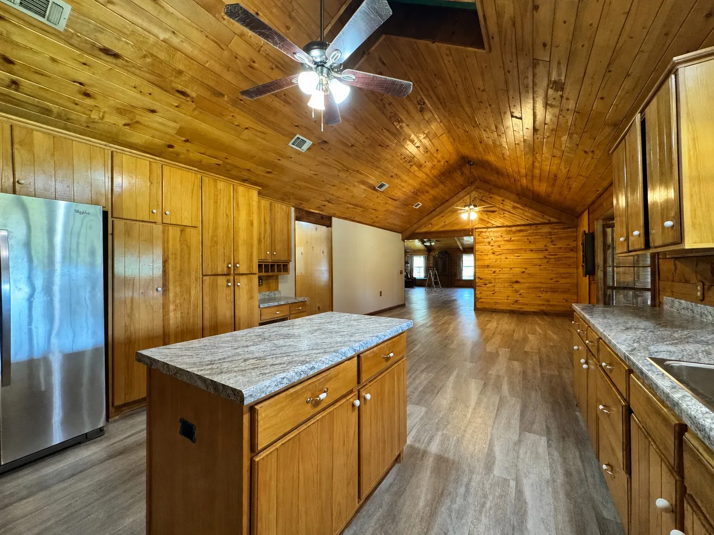 Kitchen featuring an island with stone-finish countertop, wood cabinetry, stainless steel refrigerator, and wood-finish flooring