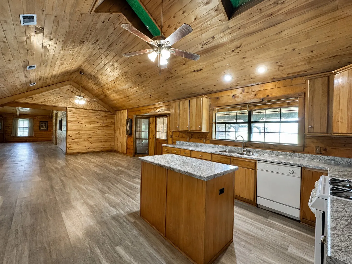 Spacious open-concept kitchen and living area featuring vaulted wood-plank ceilings, wood-finish flooring, and built-in cabinetry