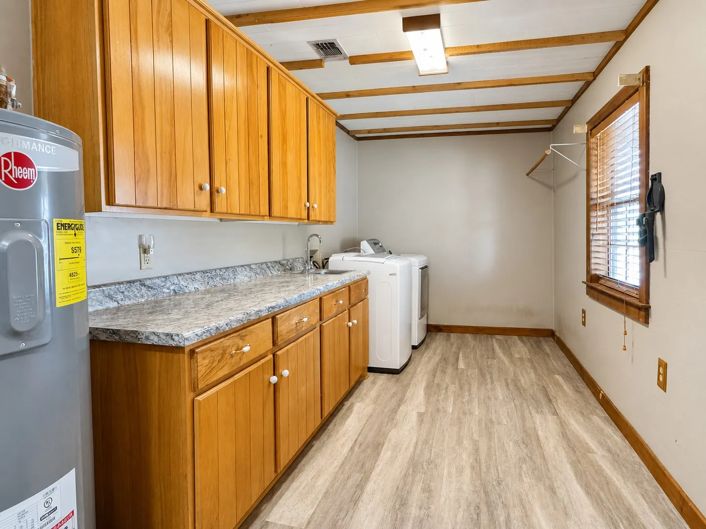 Utility room featuring light wood-finish cabinetry, a patterned countertop with an integrated sink, and light-toned wood-finish flooring