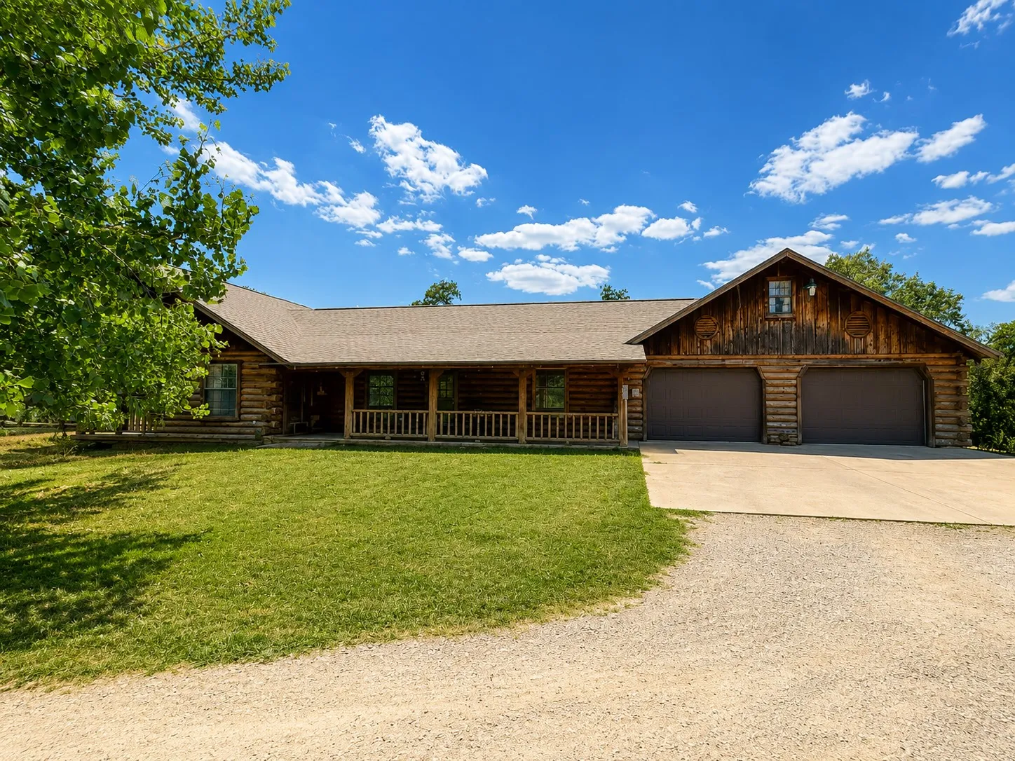 Log cabin exterior with a covered front porch, two-car garage, and an expansive lawn