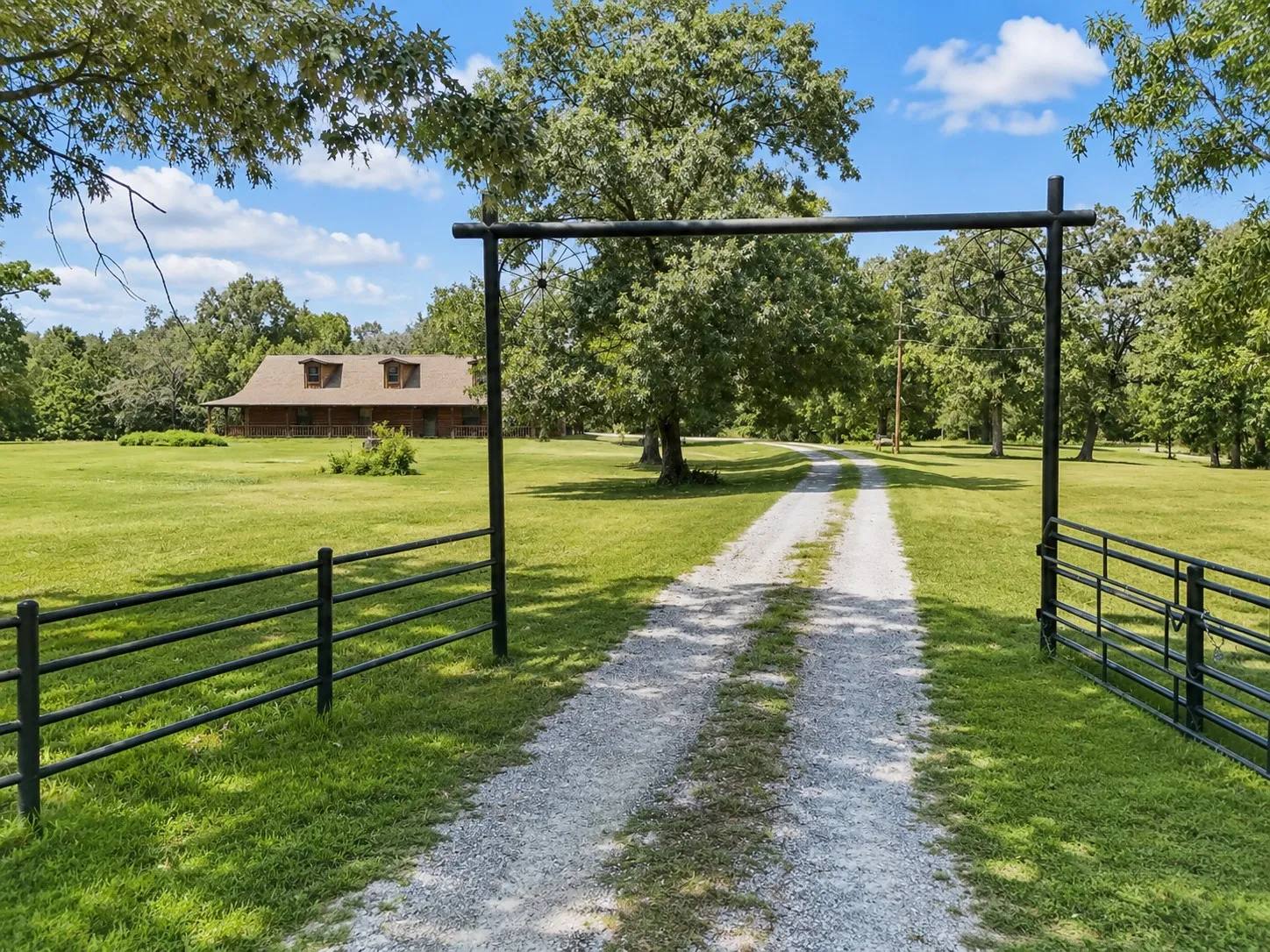 Gated entrance featuring a gravel driveway and black metal fencing