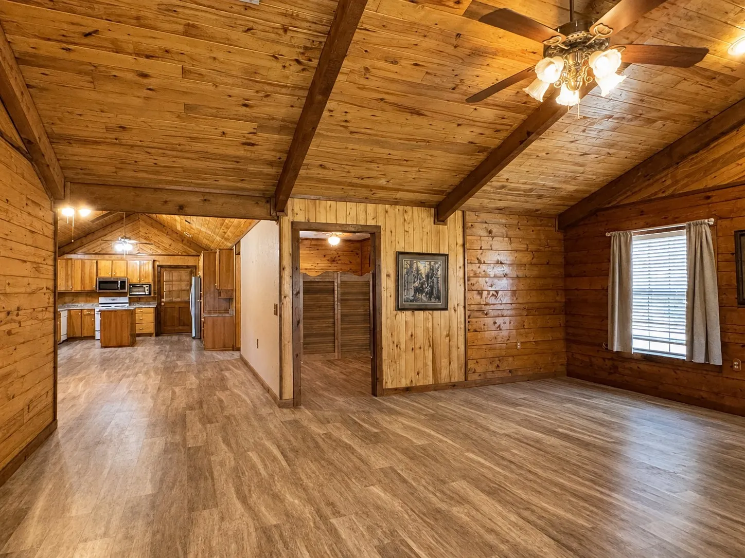 Vaulted wood-paneled ceilings with exposed beams, wood-finish flooring, a kitchen with wood cabinetry and built-in appliances, and a ceiling fan with integrated lighting