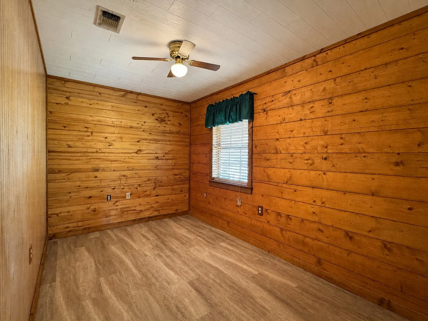 Cozy bedroom retreat showcasing warm wood-plank walls throughout, wood-finish flooring, and a ceiling fan with integrated lighting fixture