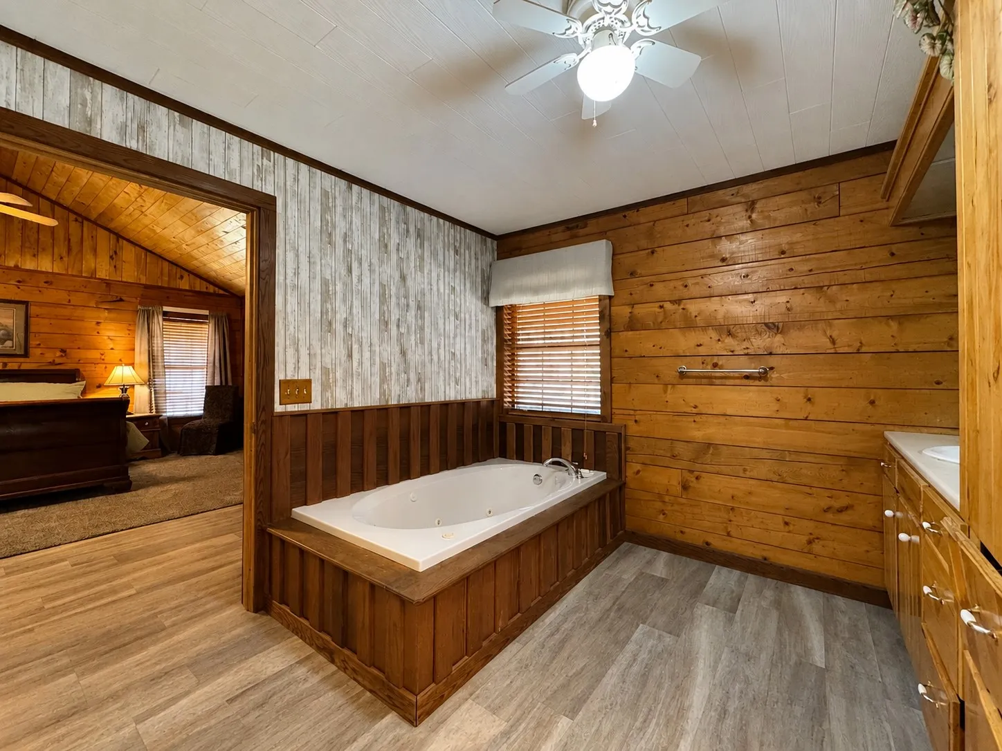 Bathroom featuring a built-in jetted tub with wood panel surround, wood-finish flooring, wood panel walls, and a vanity with built-in cabinetry and a white countertop