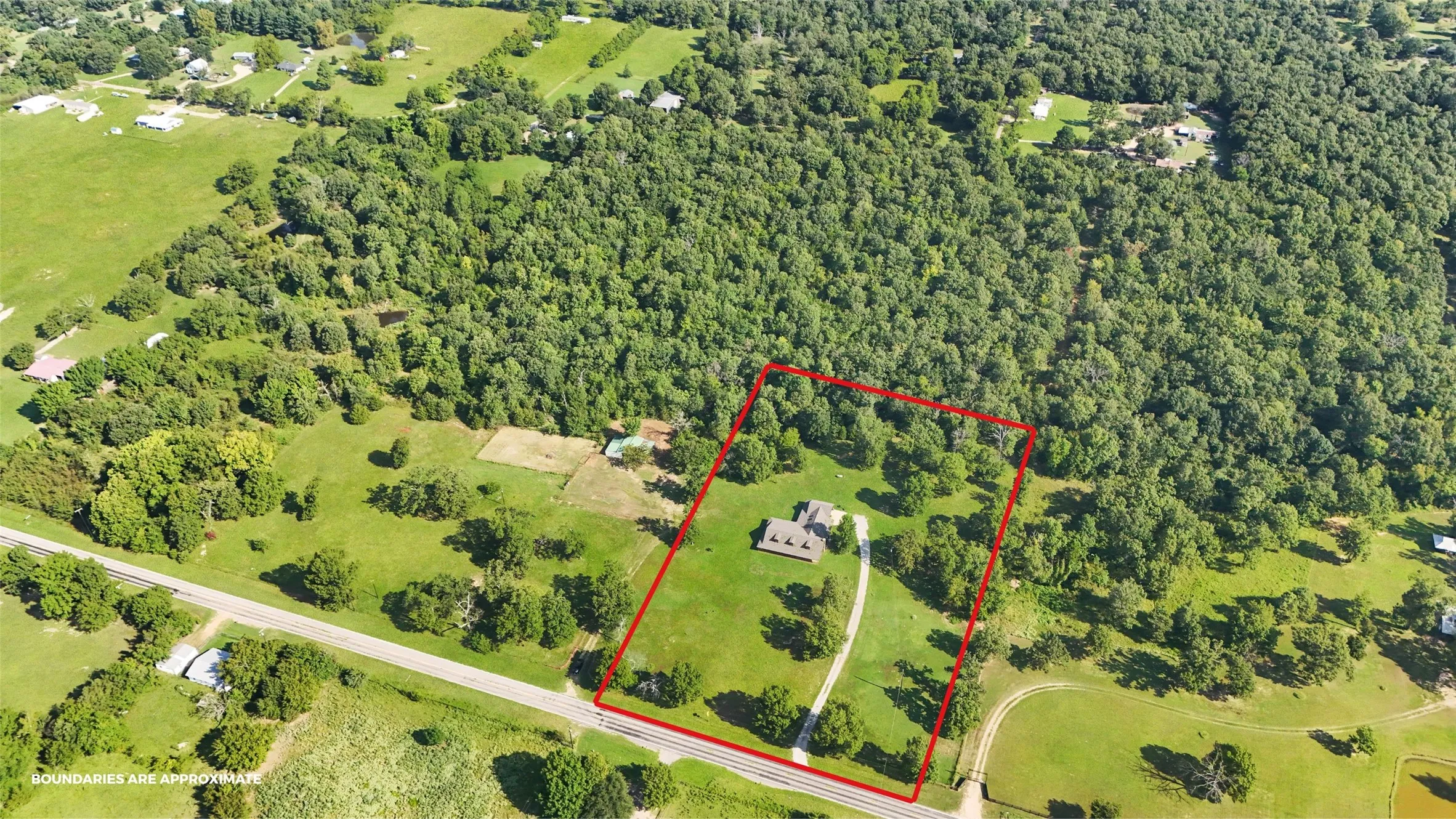 Expansive lot featuring a main residence, mature trees, open green spaces, and direct road frontage