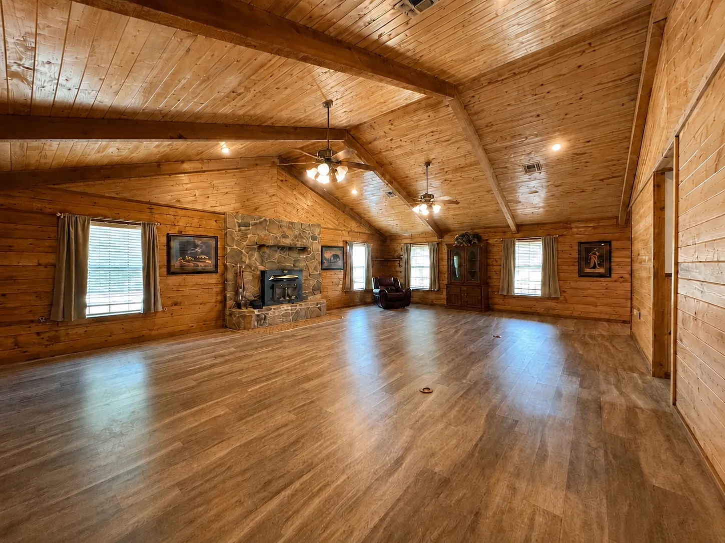 Spacious room featuring wood-finish walls and vaulted ceilings with exposed beams