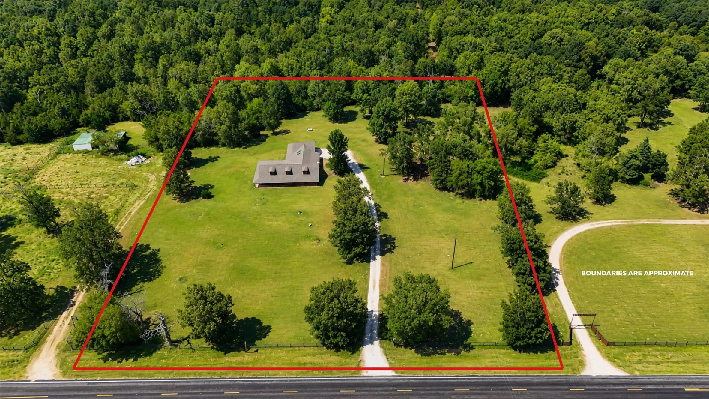 Expansive rural property featuring a manicured lawn, mature tree-lined perimeter, and a residence with a driveway approach