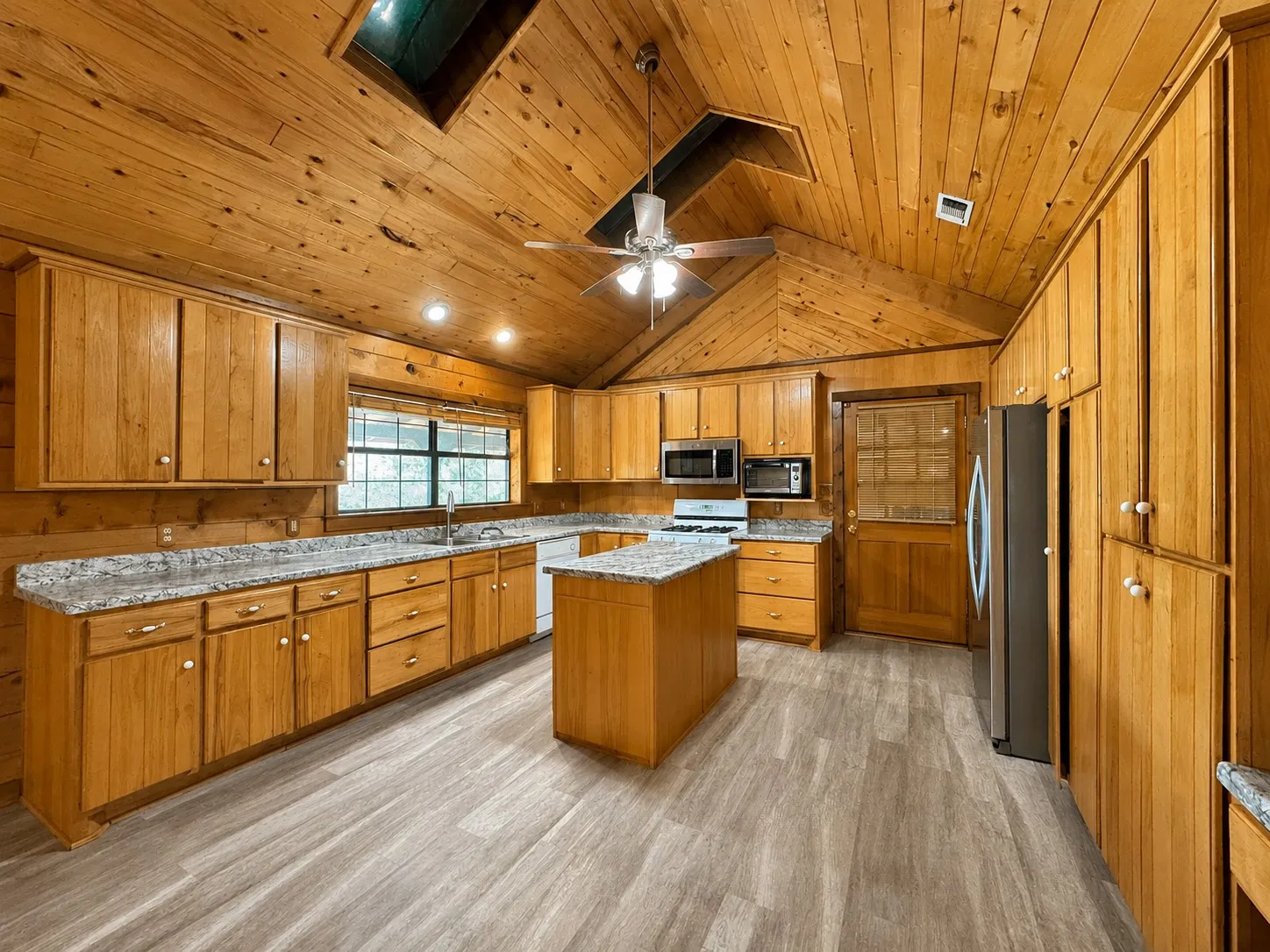 Kitchen featuring wood plank walls and ceiling, a skylight, a central island, light-toned wood cabinetry, and stainless steel appliances