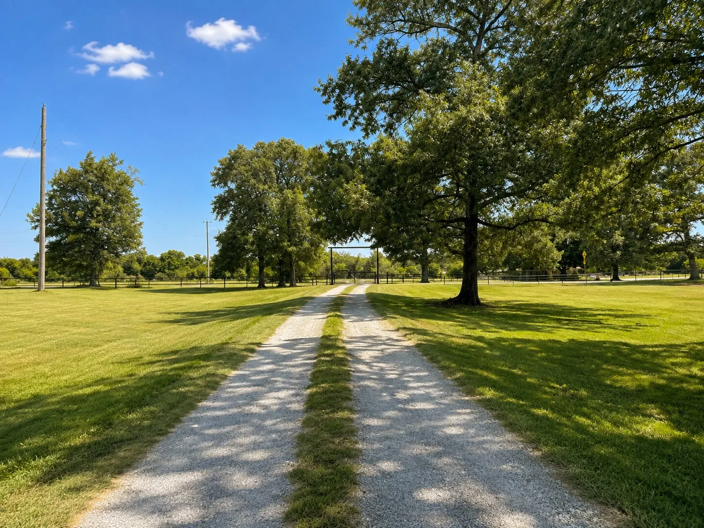 Gravel driveway flanked by expansive green lawns and mature shade trees