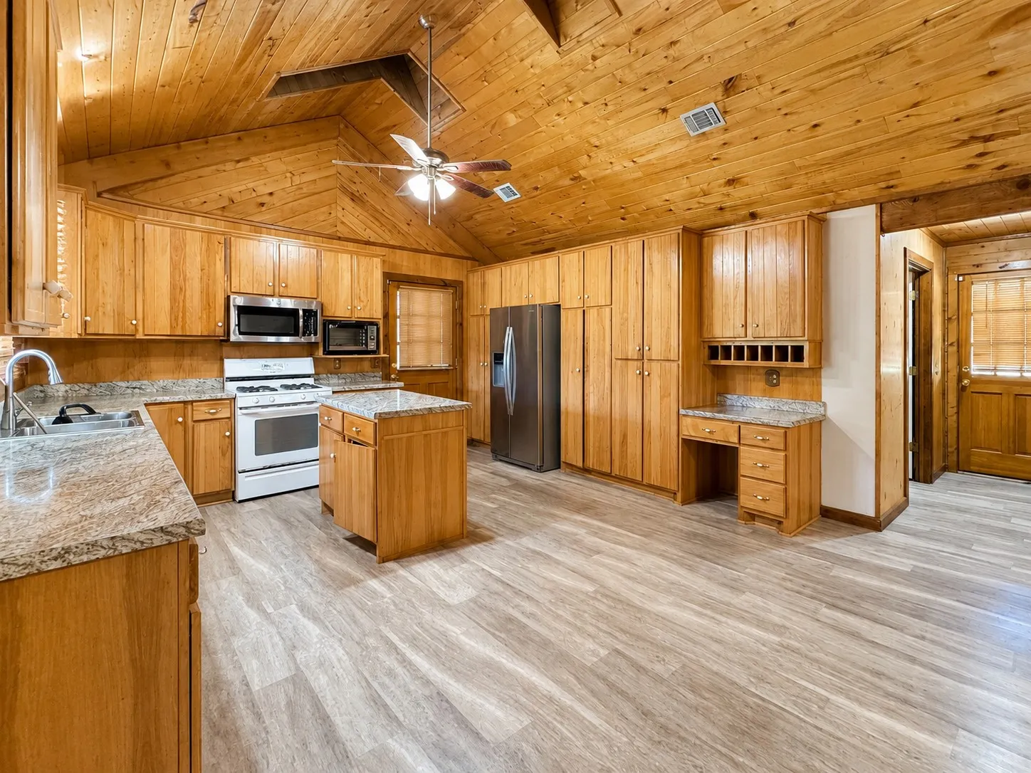 Spacious kitchen featuring extensive wood cabinetry, granite-finish countertops, stainless steel appliances, a center island, and wood-finish flooring