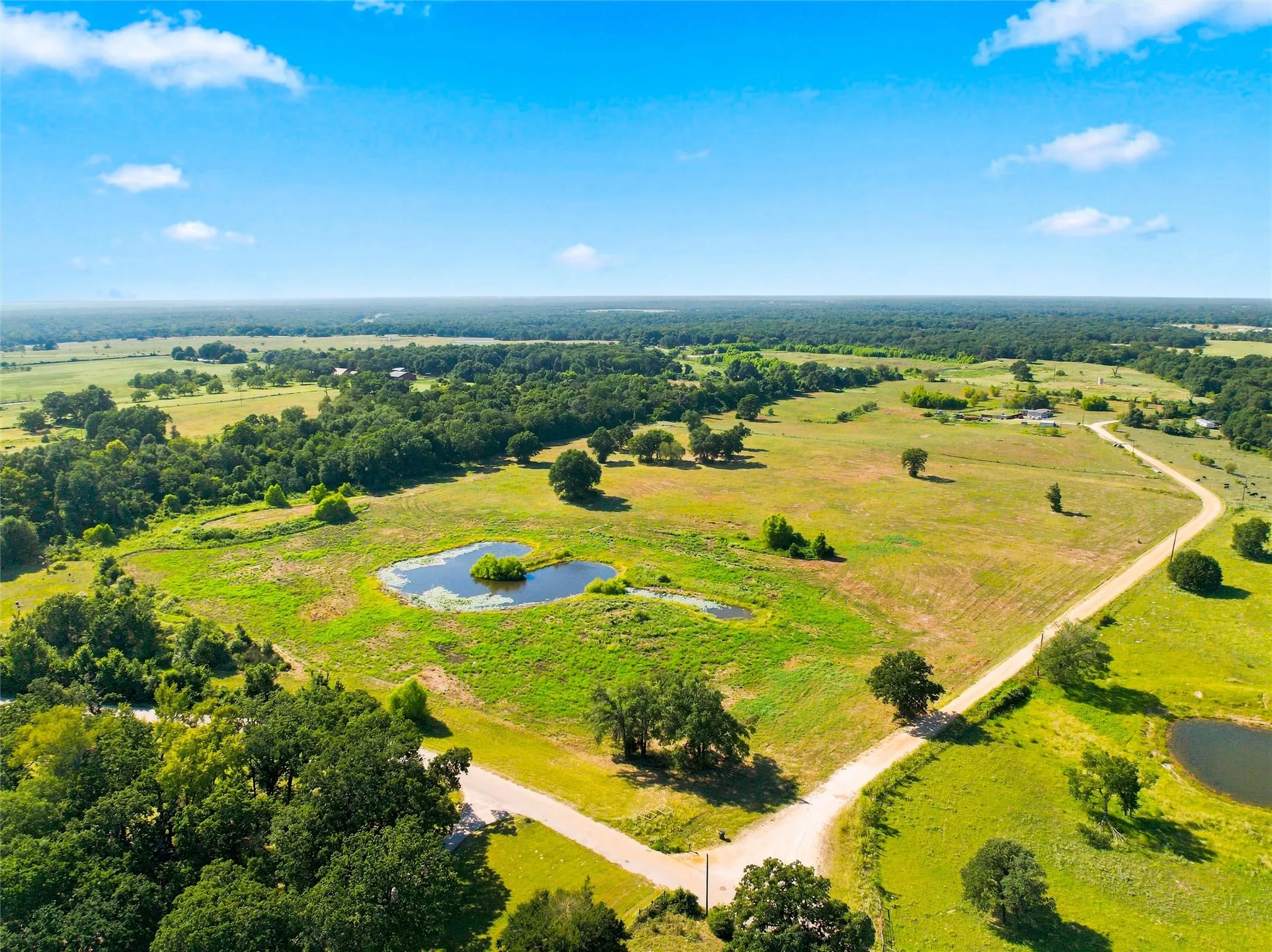 Expansive property featuring verdant fields, established trees, and multiple bodies of water