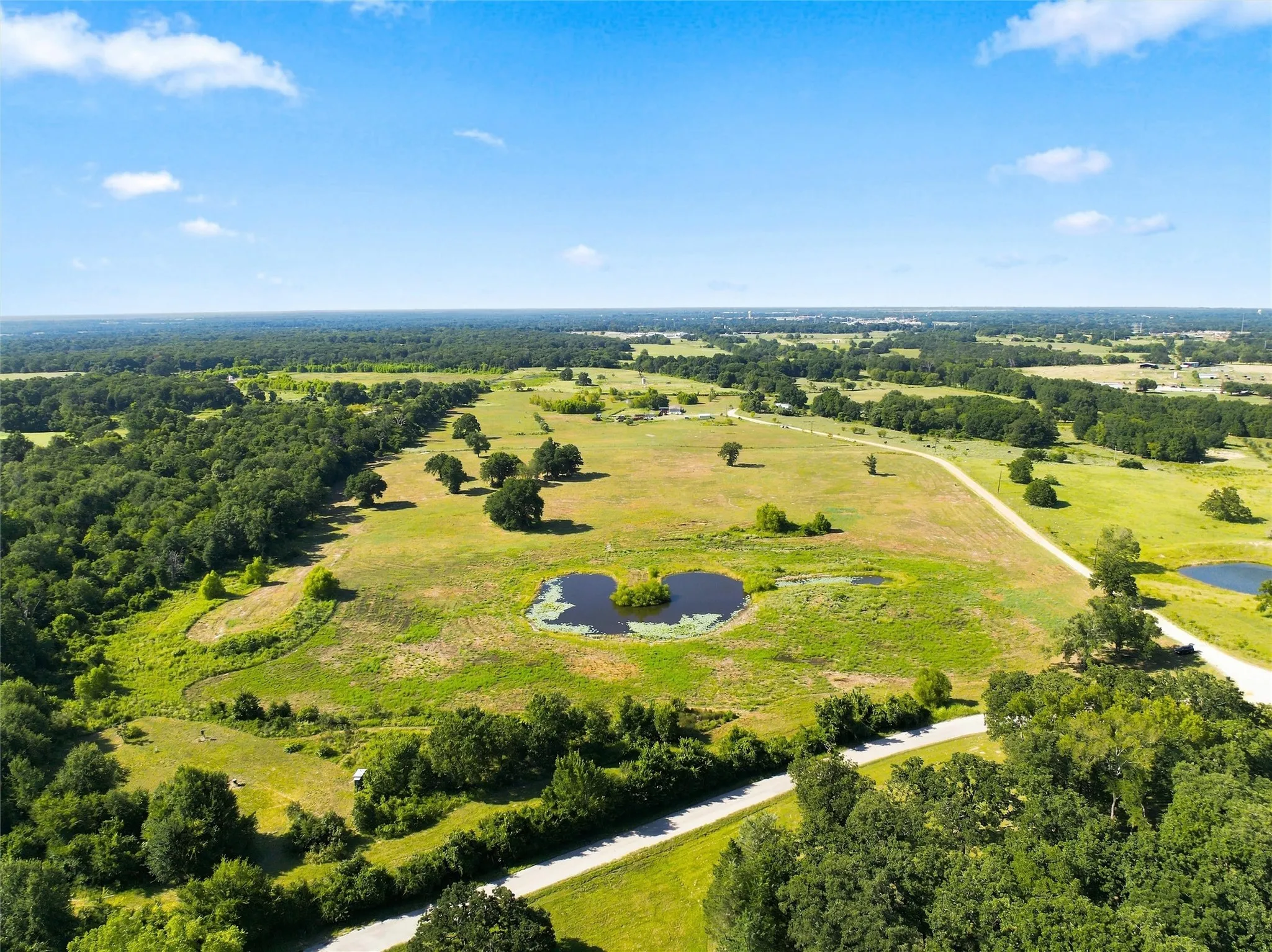 Expansive rural landscape featuring scattered trees, multiple ponds, and a winding unpaved road