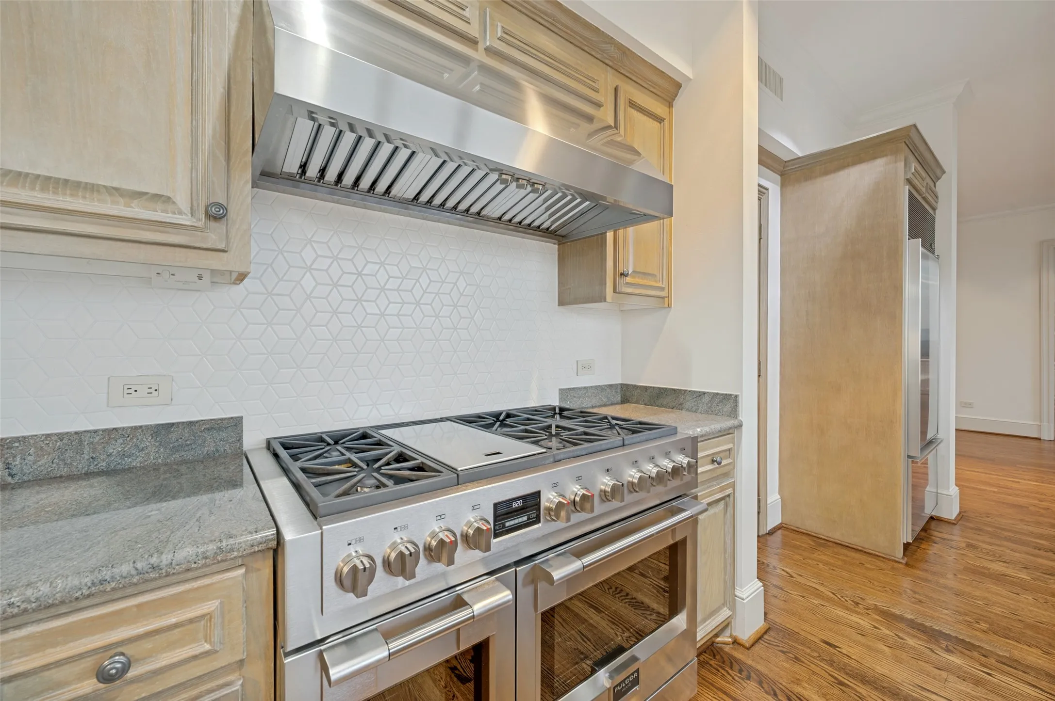 Oven with six gas burners and double ovens topped with a commercial vent hood.