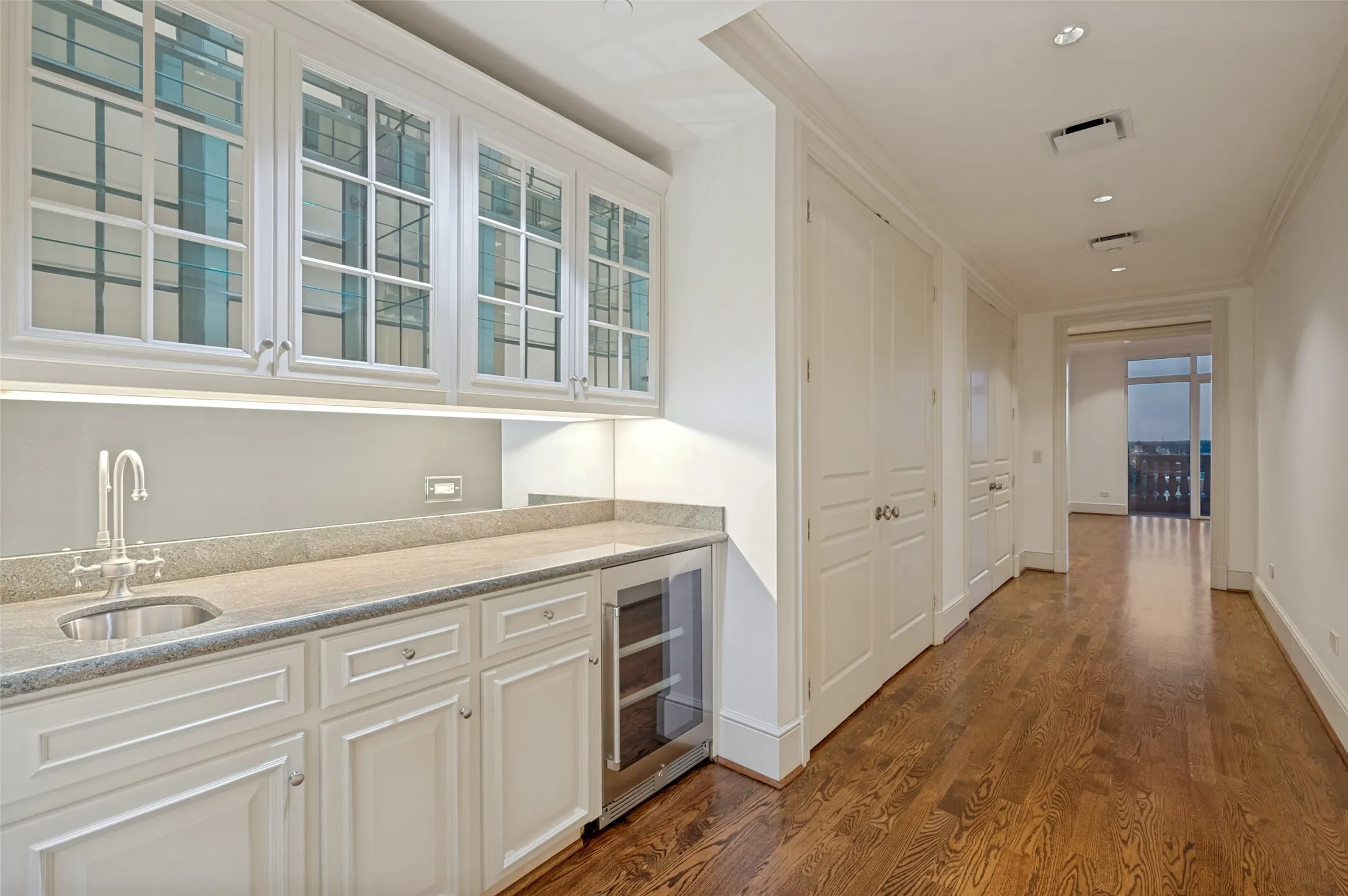 View from foyer to central interior hallway with wet bar, glass cabinets and mini-fridge.