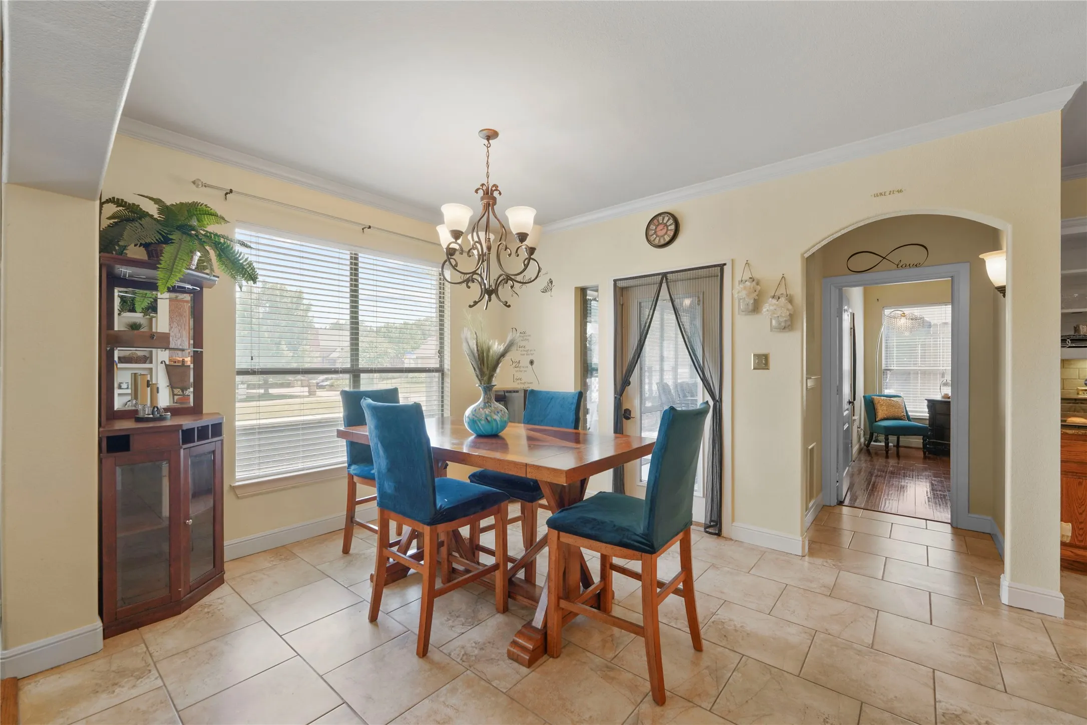 Bright dining area featuring tile flooring, a wood-finish dining table with upholstered chairs, and a decorative chandelier