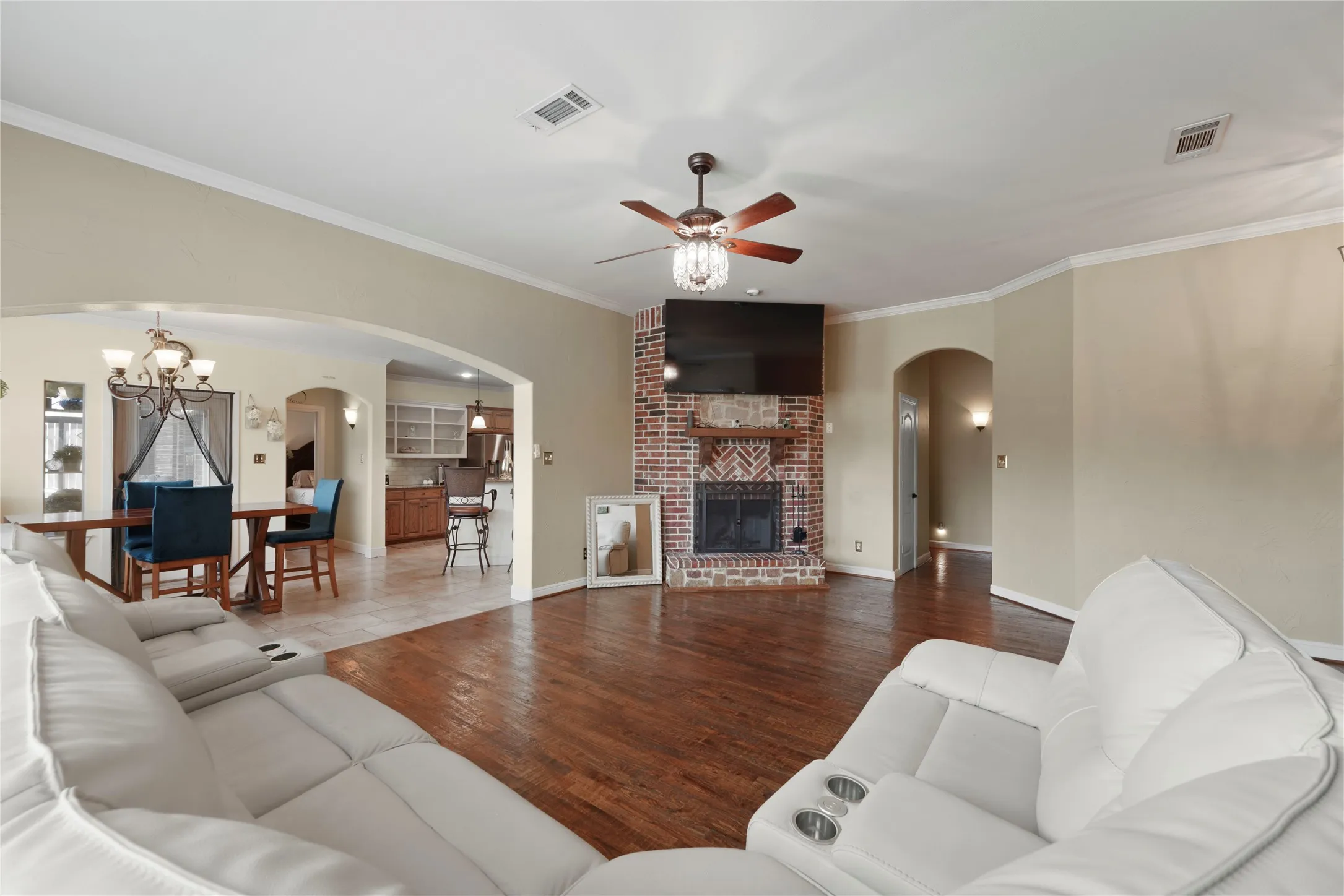 Living area featuring wood-finish flooring, a brick fireplace, and a ceiling fan with integrated lighting