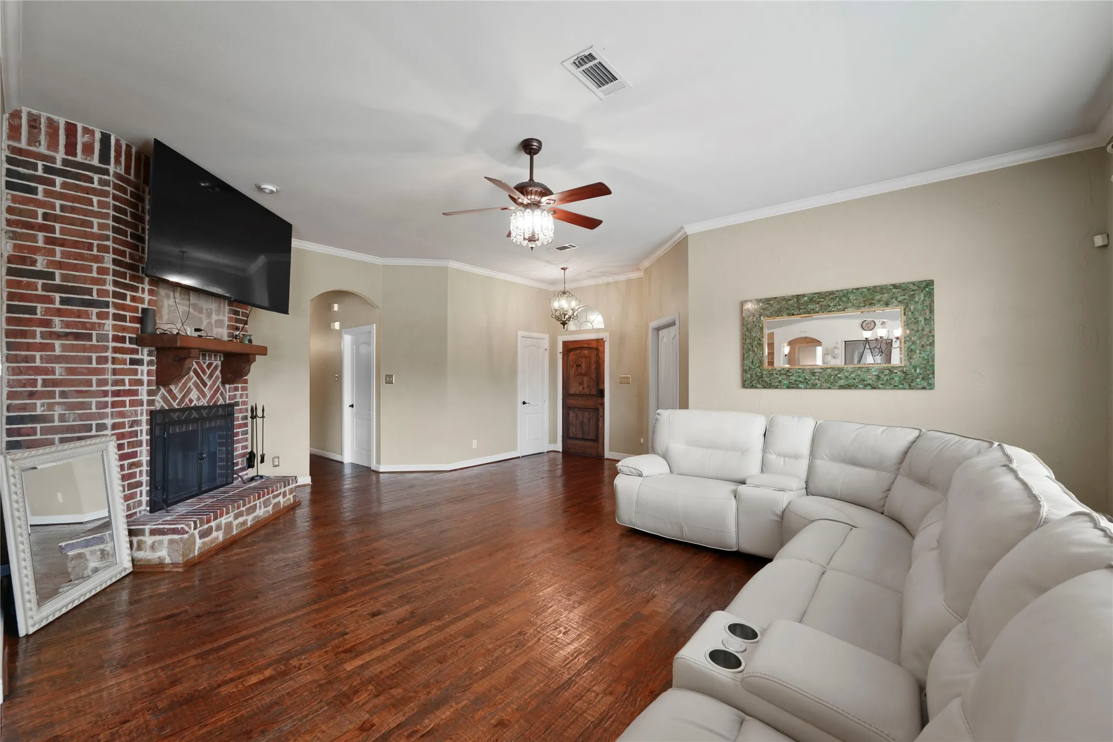 Brick-faced fireplace with a wood mantle, rich wood-finish flooring, and a ceiling fan with integrated lighting