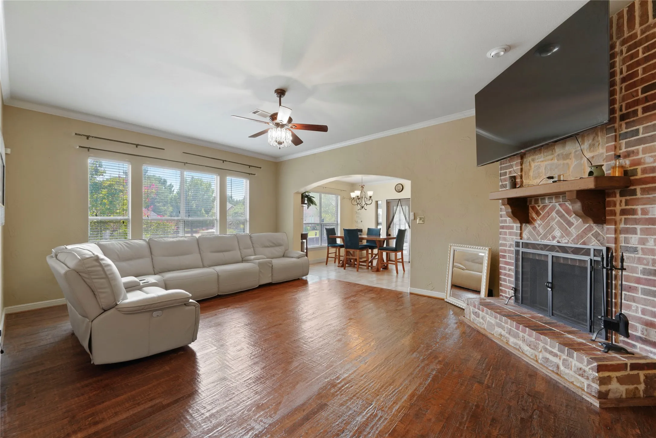 Expansive room featuring wood-finish flooring, a brick fireplace with a wood mantel, a ceiling fan, and multiple windows