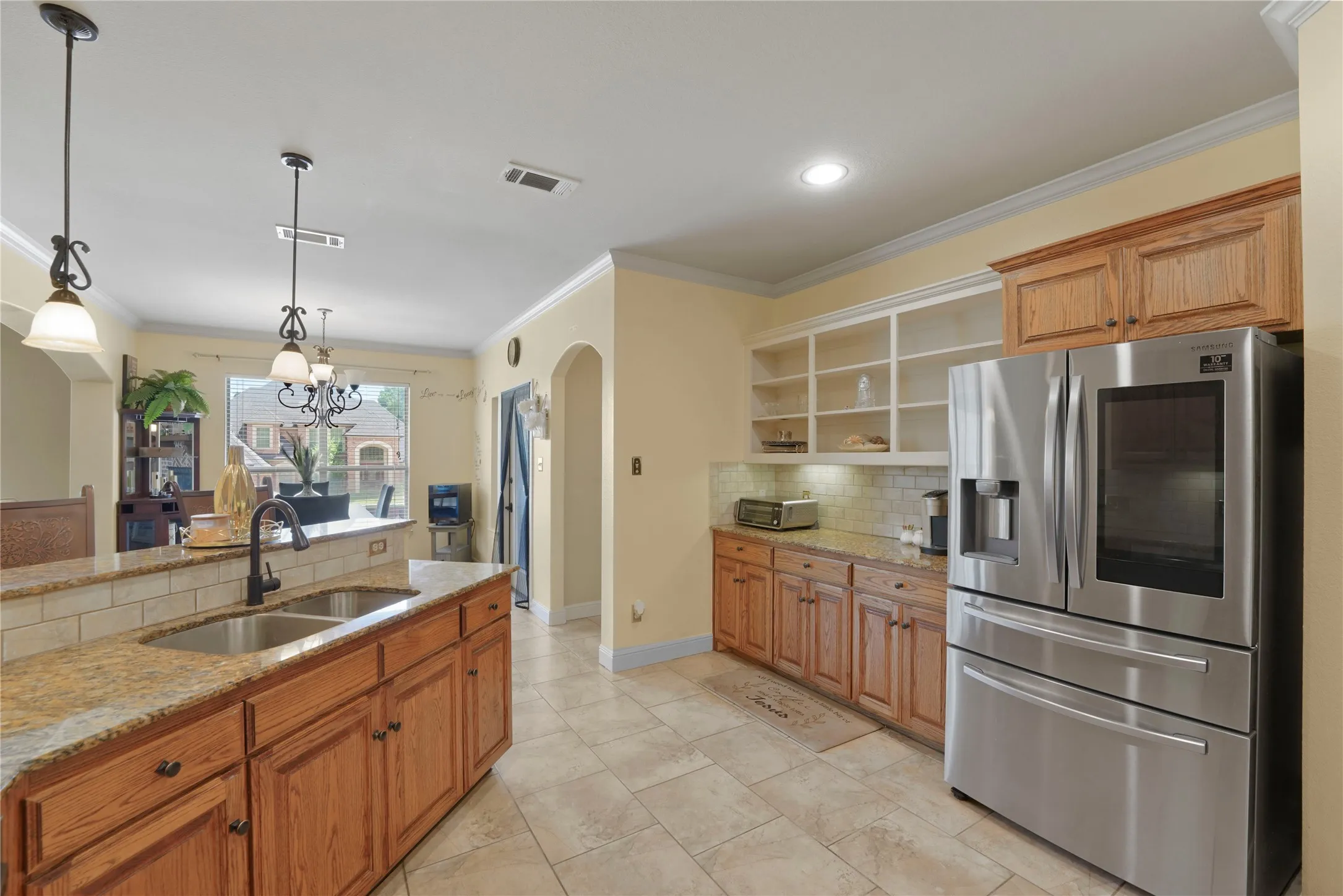 Kitchen featuring a large island with dual basin sink, light-toned cabinetry, tile flooring, built-in shelving, and recessed lighting